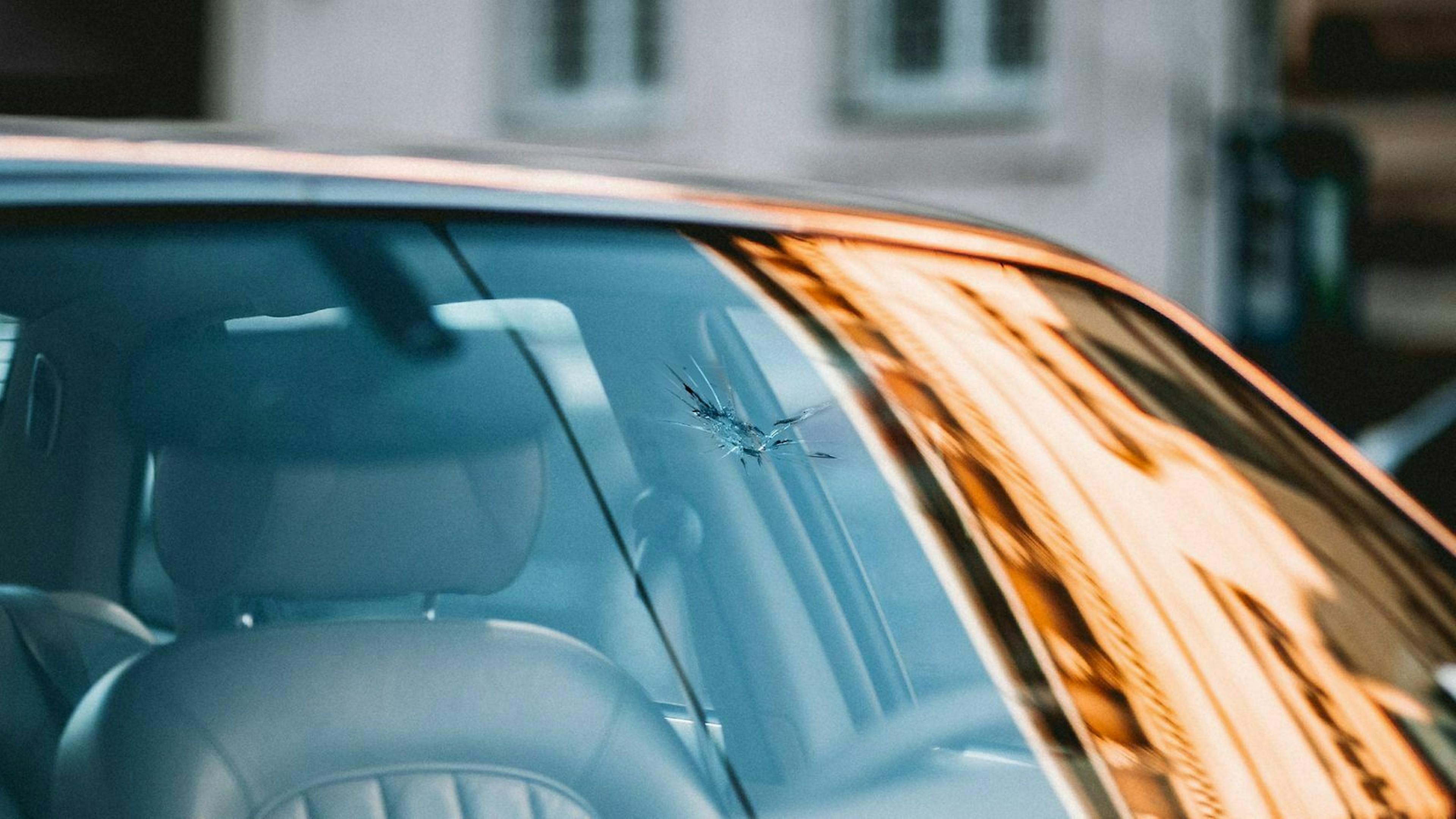 In der Abendsonne steht ein Auto auf dessen Wundschutzscheibe ein Steinschlag zu sehen ist.