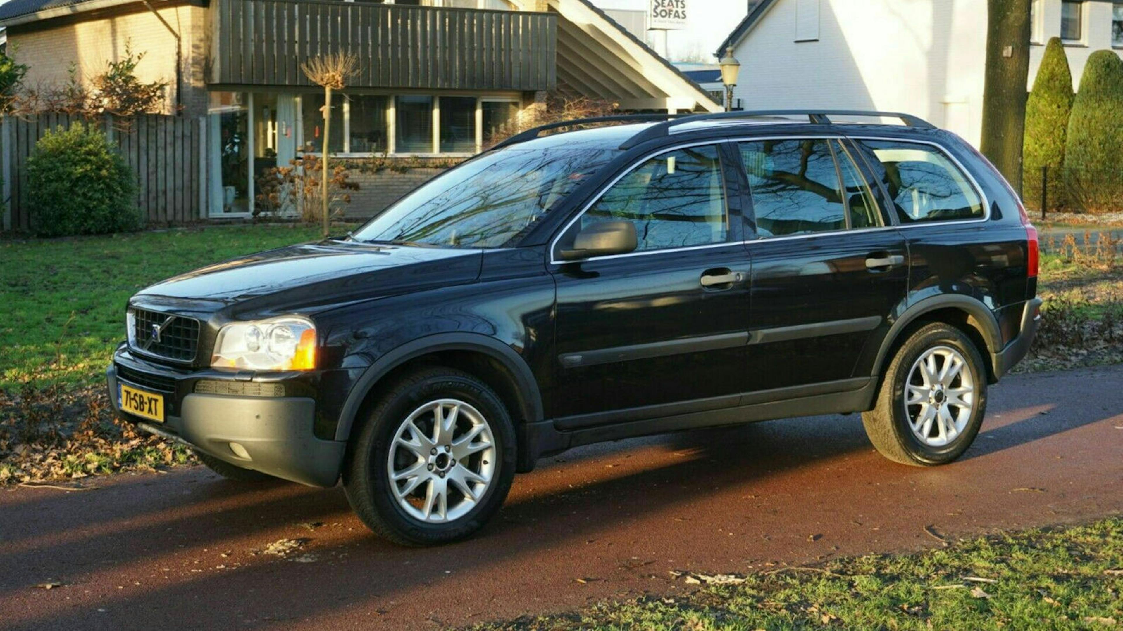 Ein schwarzer Volvo XC90 steht in einer Einfahrt vor einem Wohnhaus