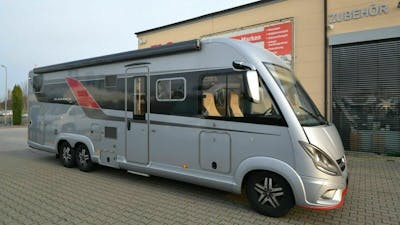 Ein silbernes Bürstner Elegance Wohnmobil steht vor einem gelben Gebäude.