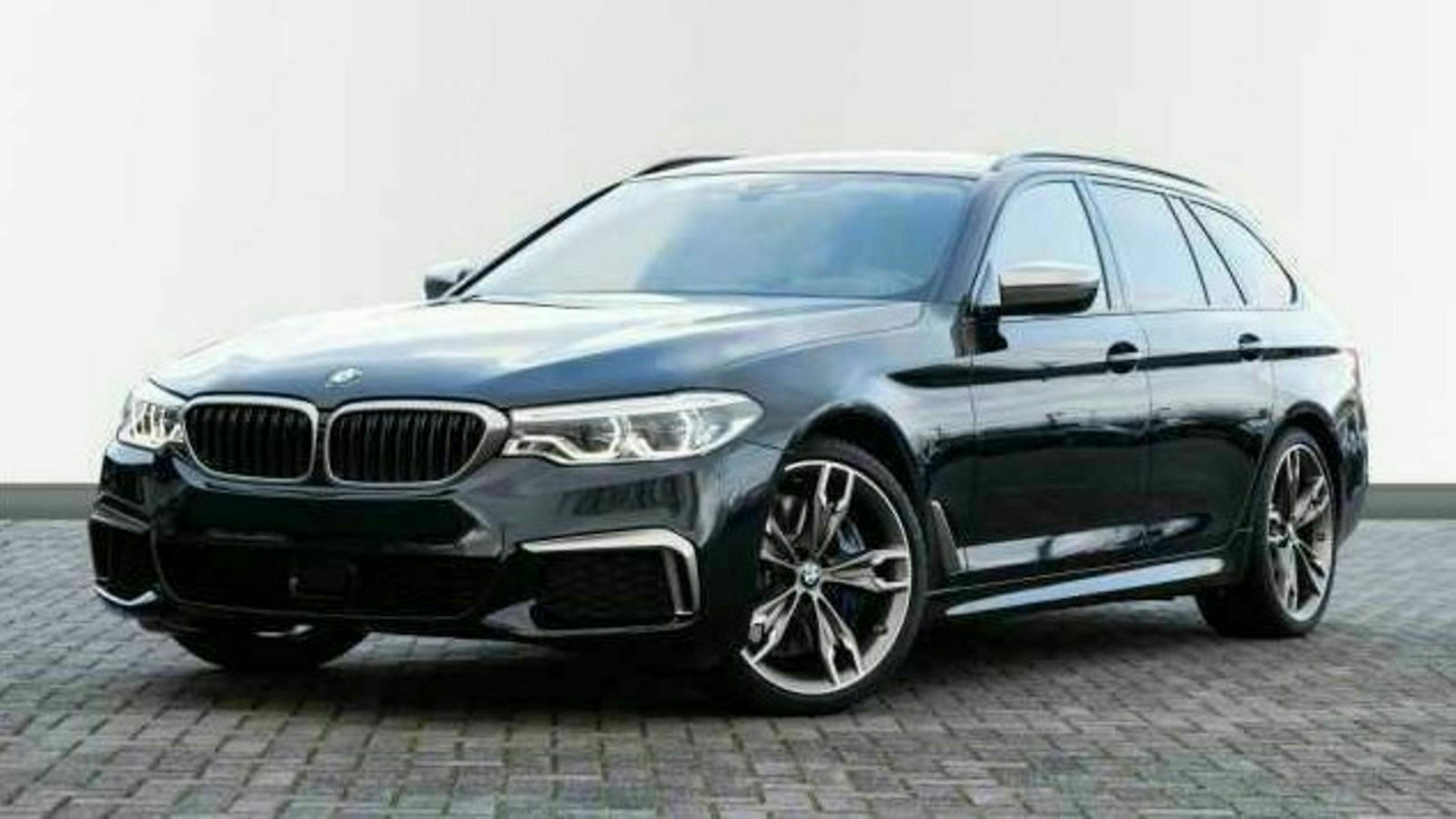Schwarzer BMW Kombi auf gepflastertem Parkplatz, seitliche Vorderansicht. Elegantes Design mit markanten Scheinwerfern und Aluminiumfelgen.