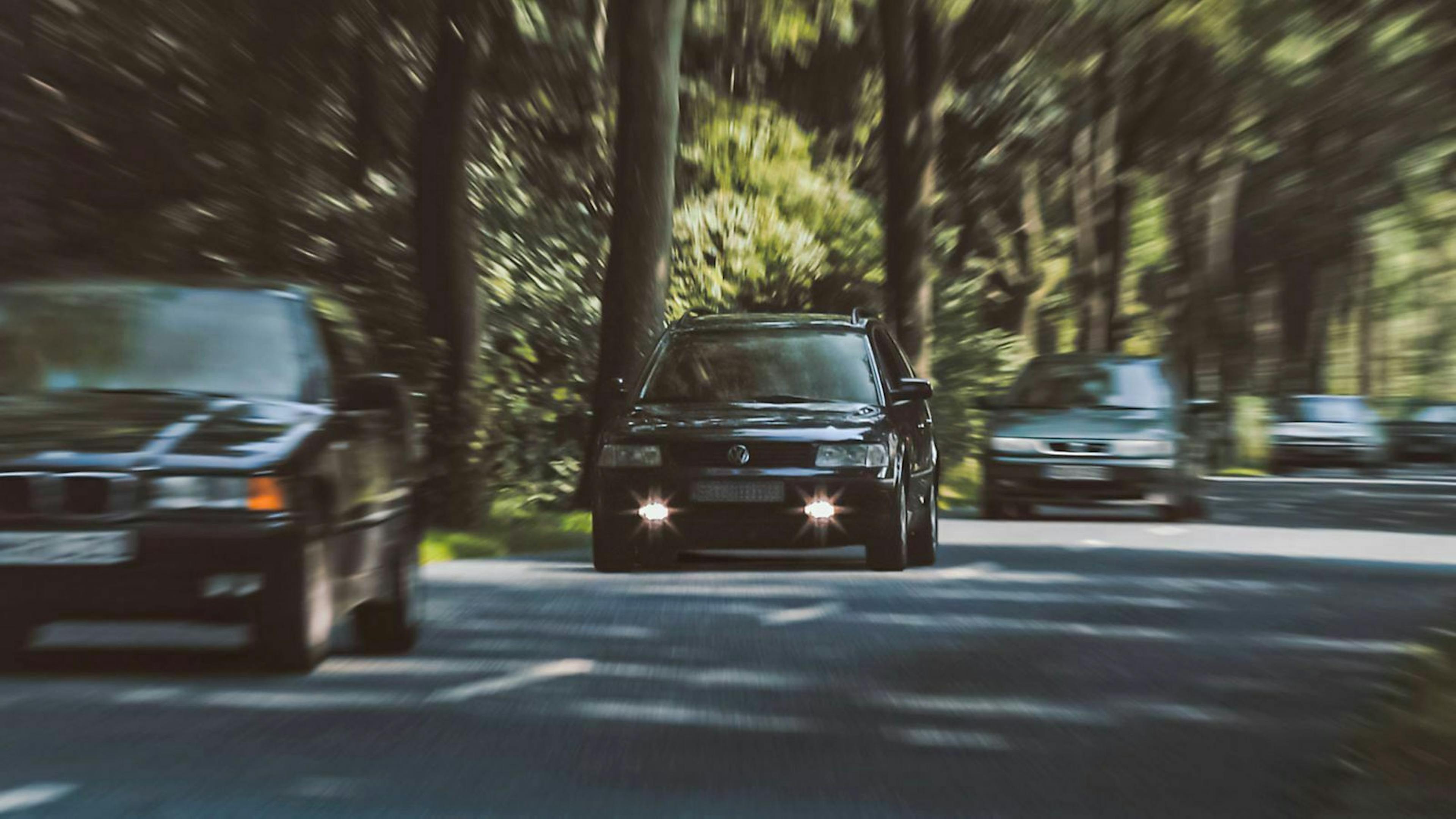 Ein VW Passat älteren Baujahrs ist auf einer Allee unterwegs. Seine Tagfahrlichter machen ihn besser erkennbar als andere Autos.