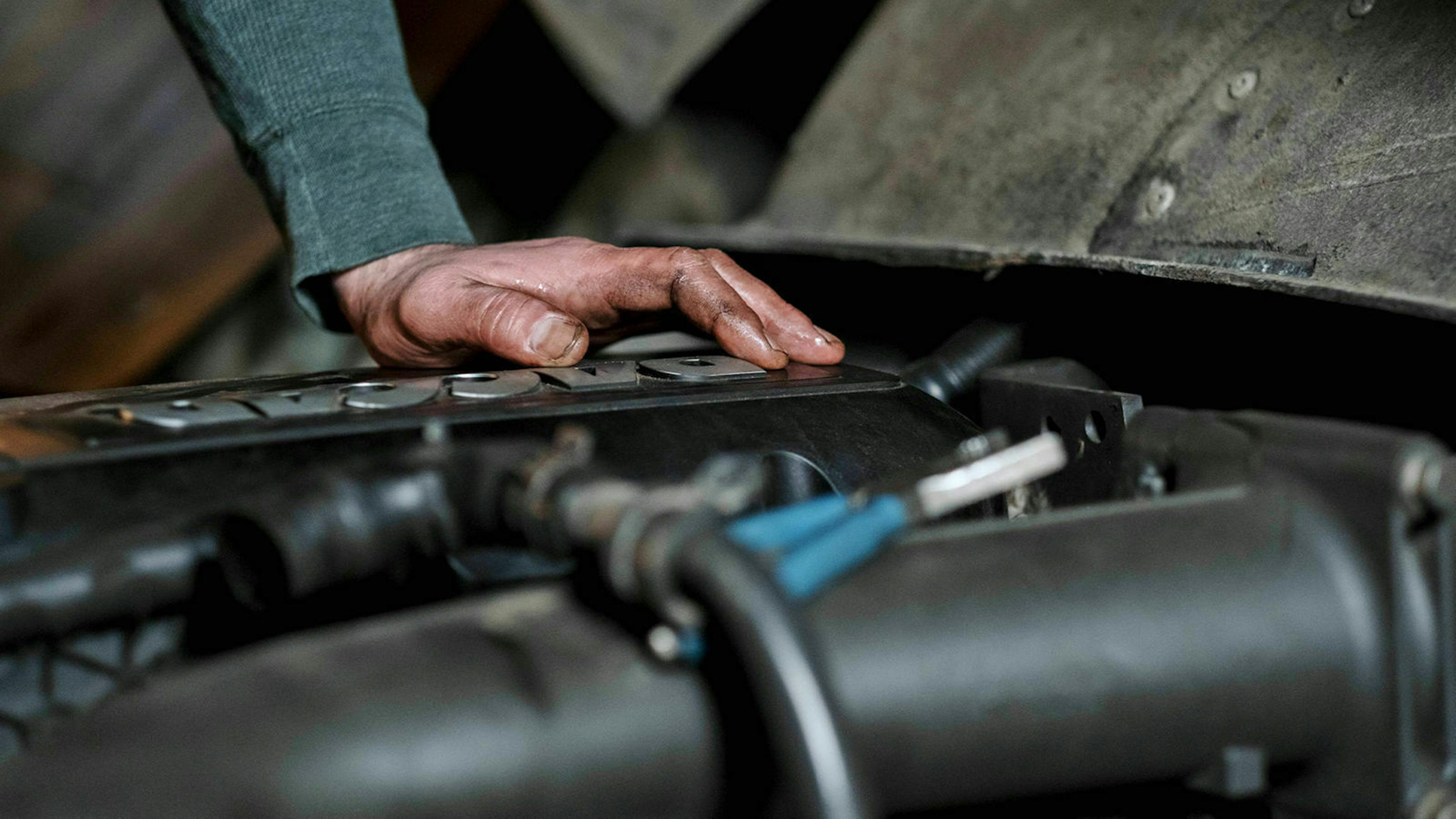 Detailaufnahme einer geöffneten Pkw-Motorhaube, auf deren Seite eine ölverschmierte Hand gestützt ist
