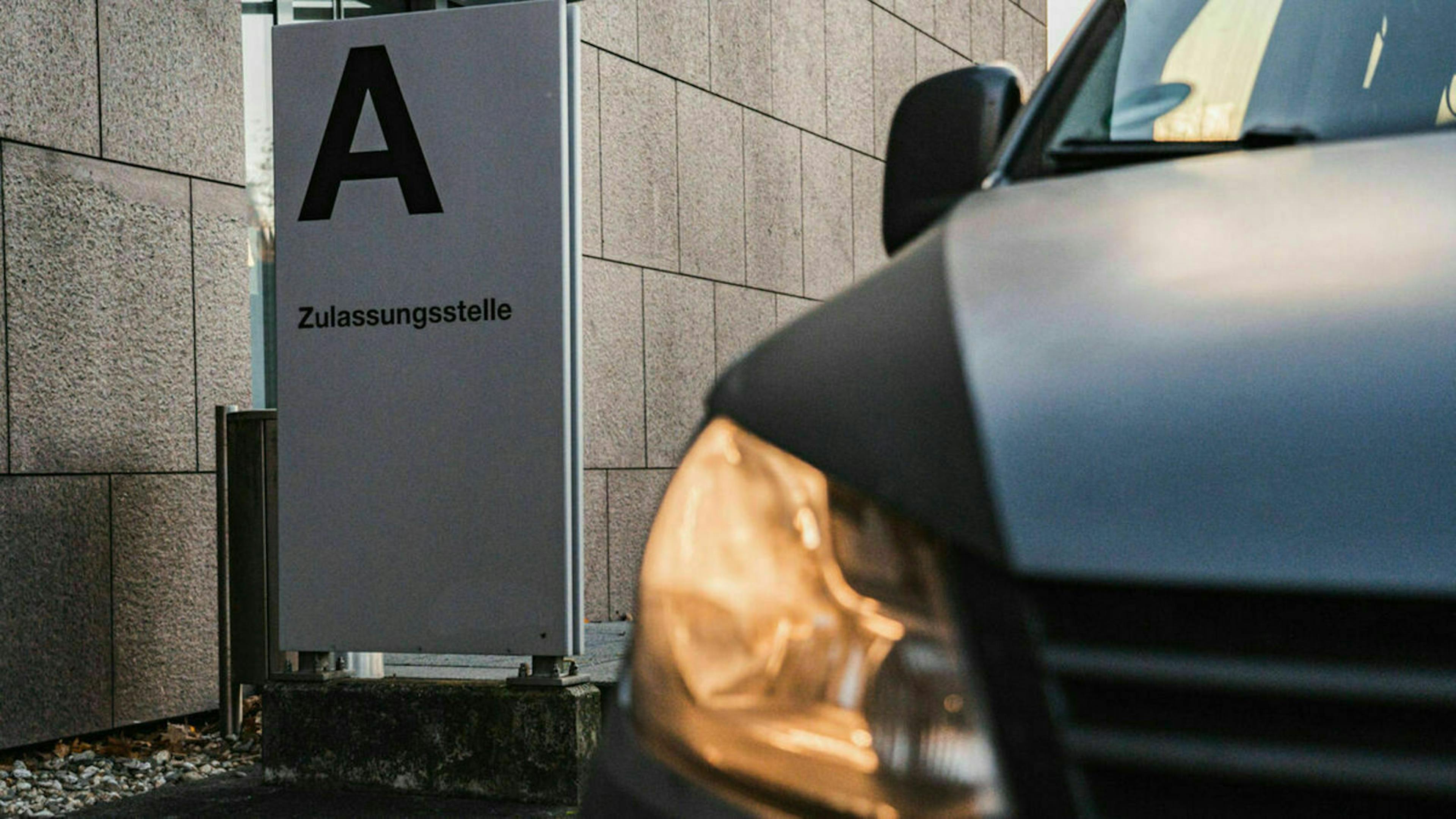 Detail eines grauen PKW, der vor dem Eingangsbereich einer Kfz-Zulassungsstelle steht 