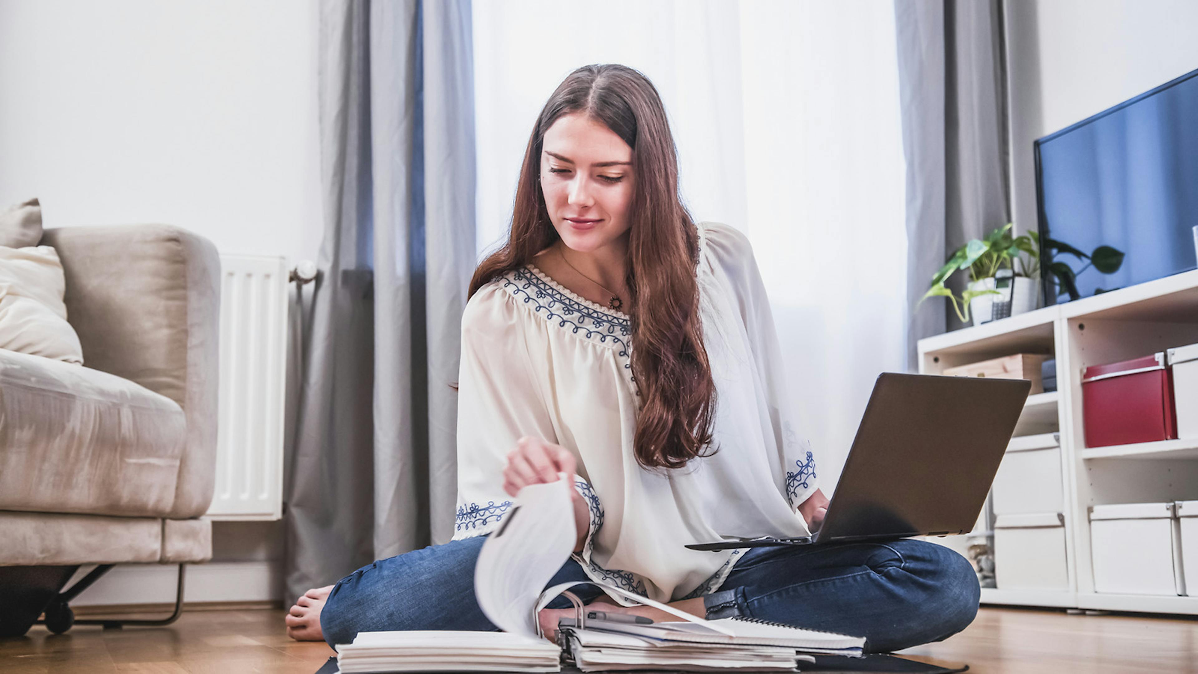 Eine Frau sitzt im Schneidersitz auf dem Boden und liest sich durch Aktenordner.
