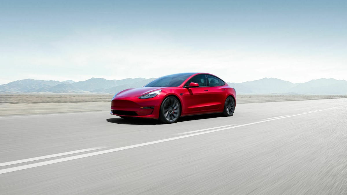 Ein rotes Tesla Model 3 mit Heckantrieb fährt eine Straße entlang