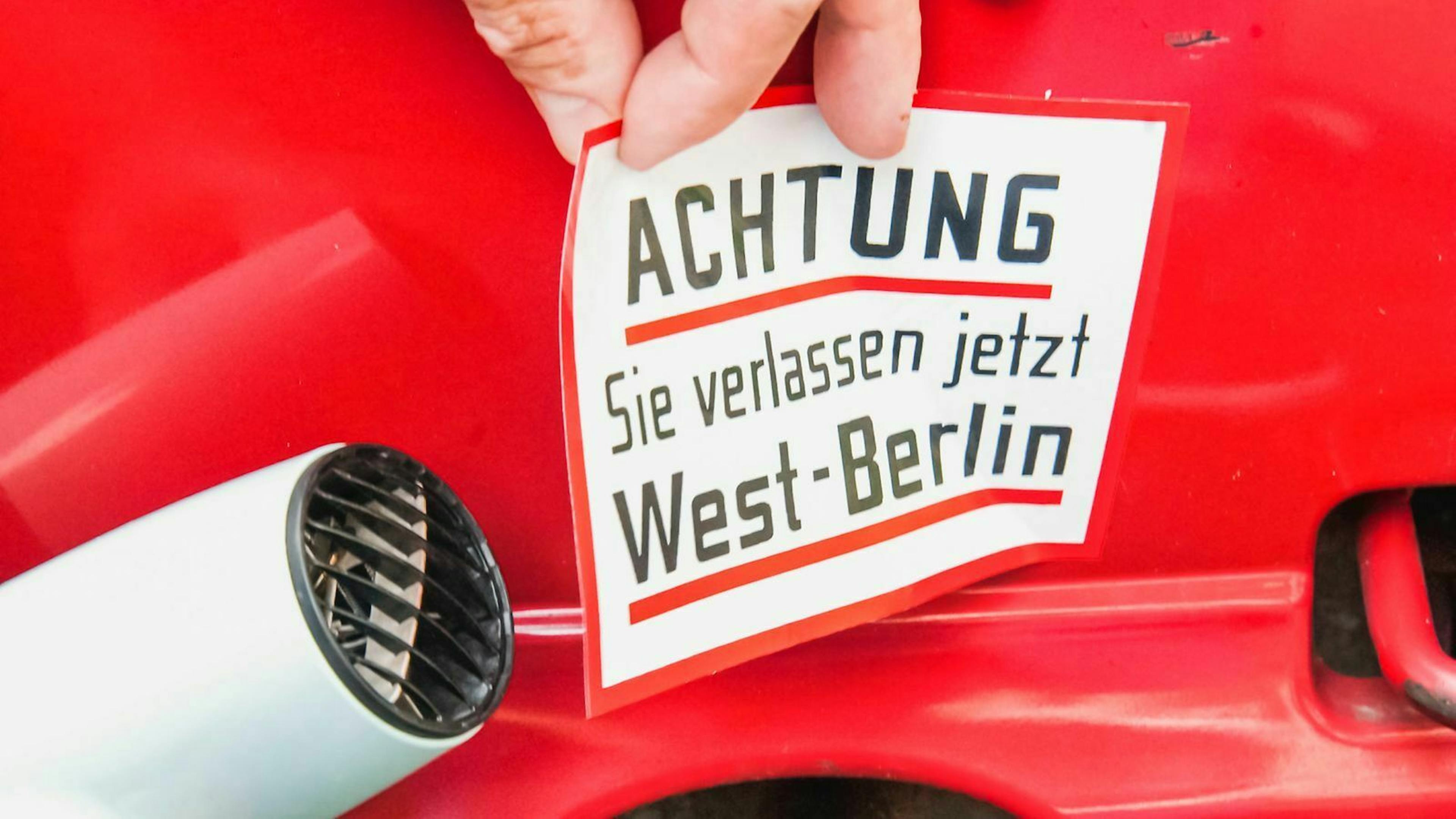 Jemand zieht mit Hilfe eines Föhns einen alten Aufkleber von einem Auto.