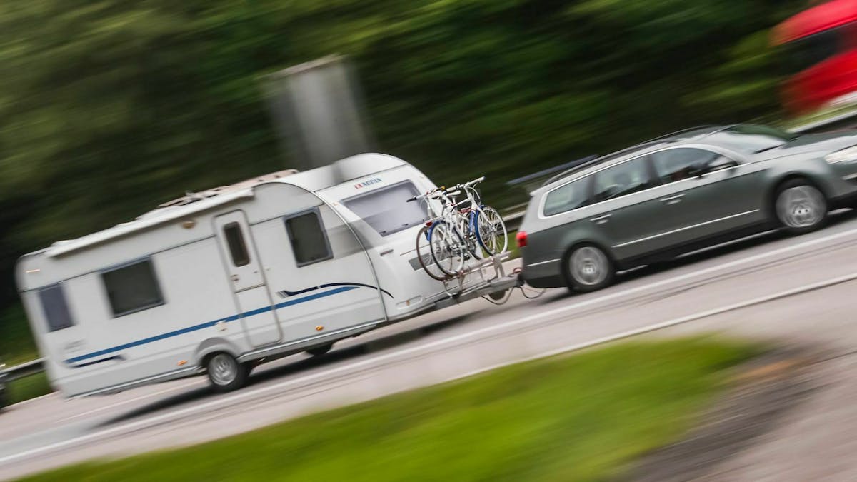 Ein Wohnanhänger wird von einem grauen VW Passat Kombi gezogen.