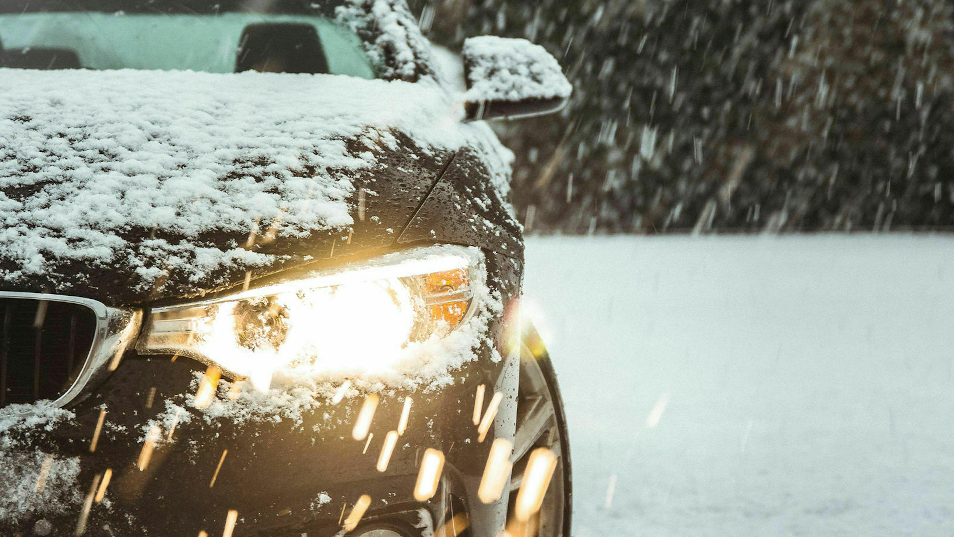 Nahaufnahme eines schwarzen PKW mit eingeschaltetem Scheinwerfer, der in einer verschneiten Landschaft steht