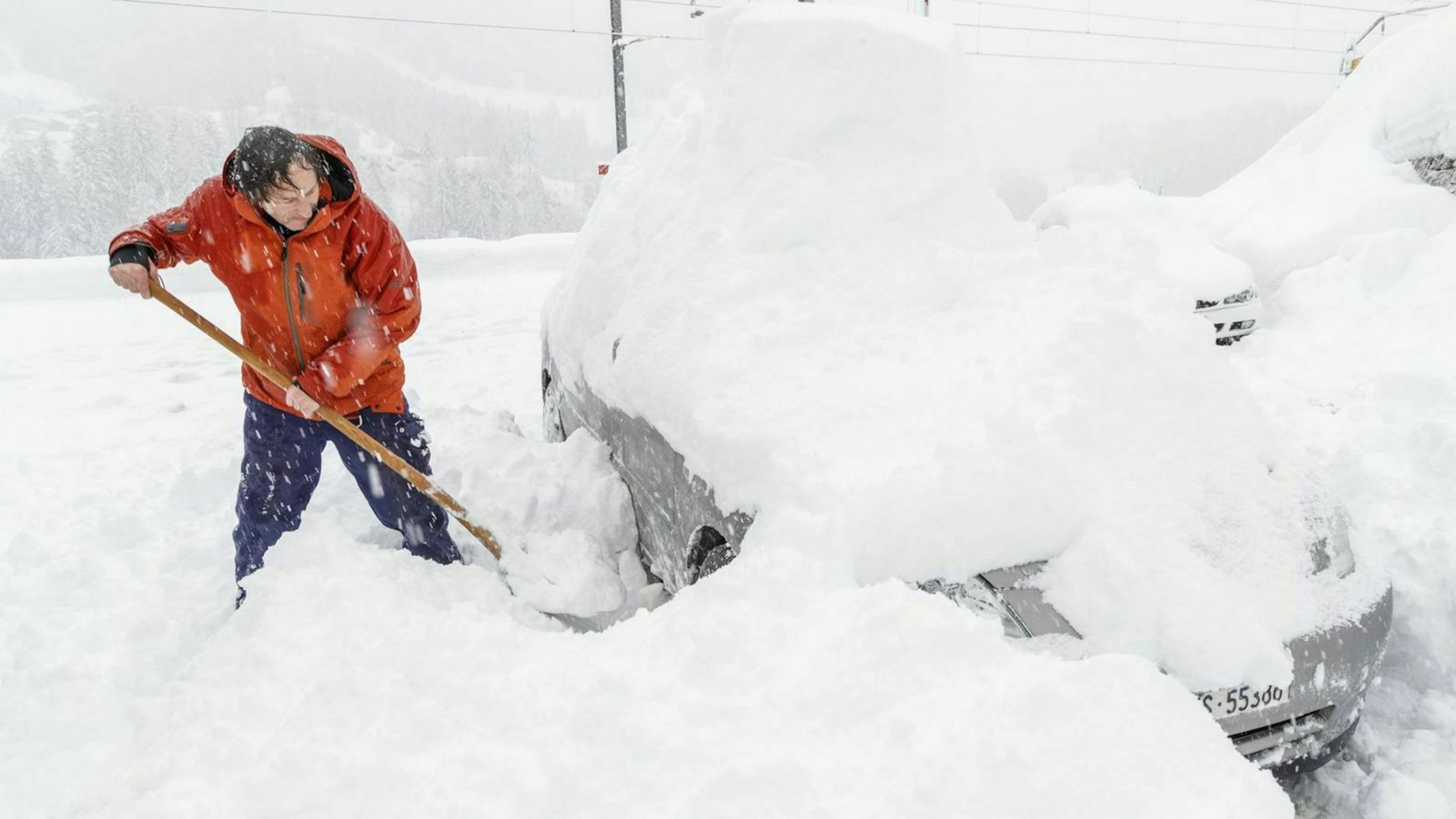 Zu sehen ist ein Mann, der sein Auto freischippt