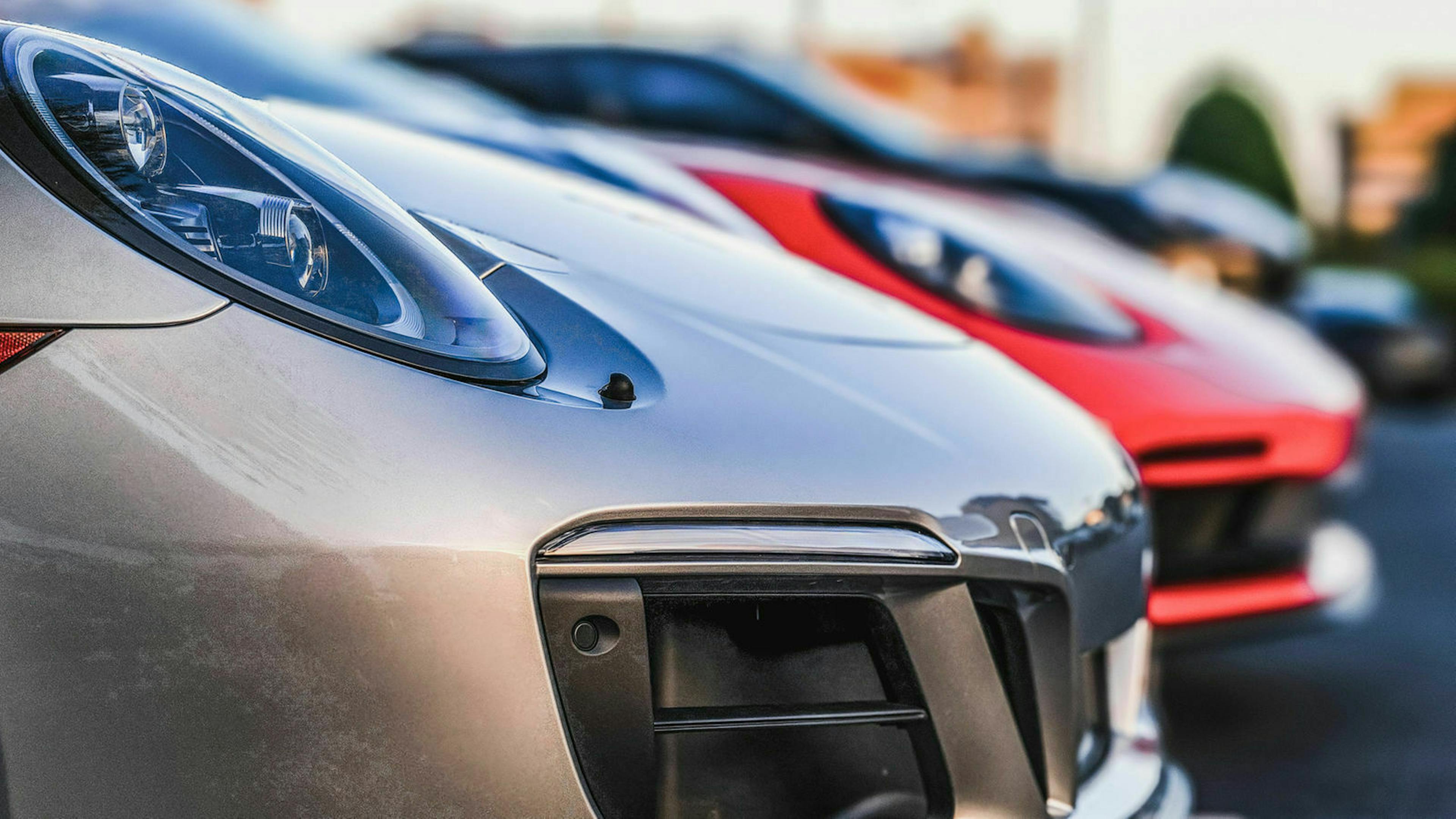 Auf dem Hof eines Gebrauchtwagenhändlers stehen zwei Porsche in Reihe geparkt. Die Fahrzeuge sind in Nahaufnahme zu sehen