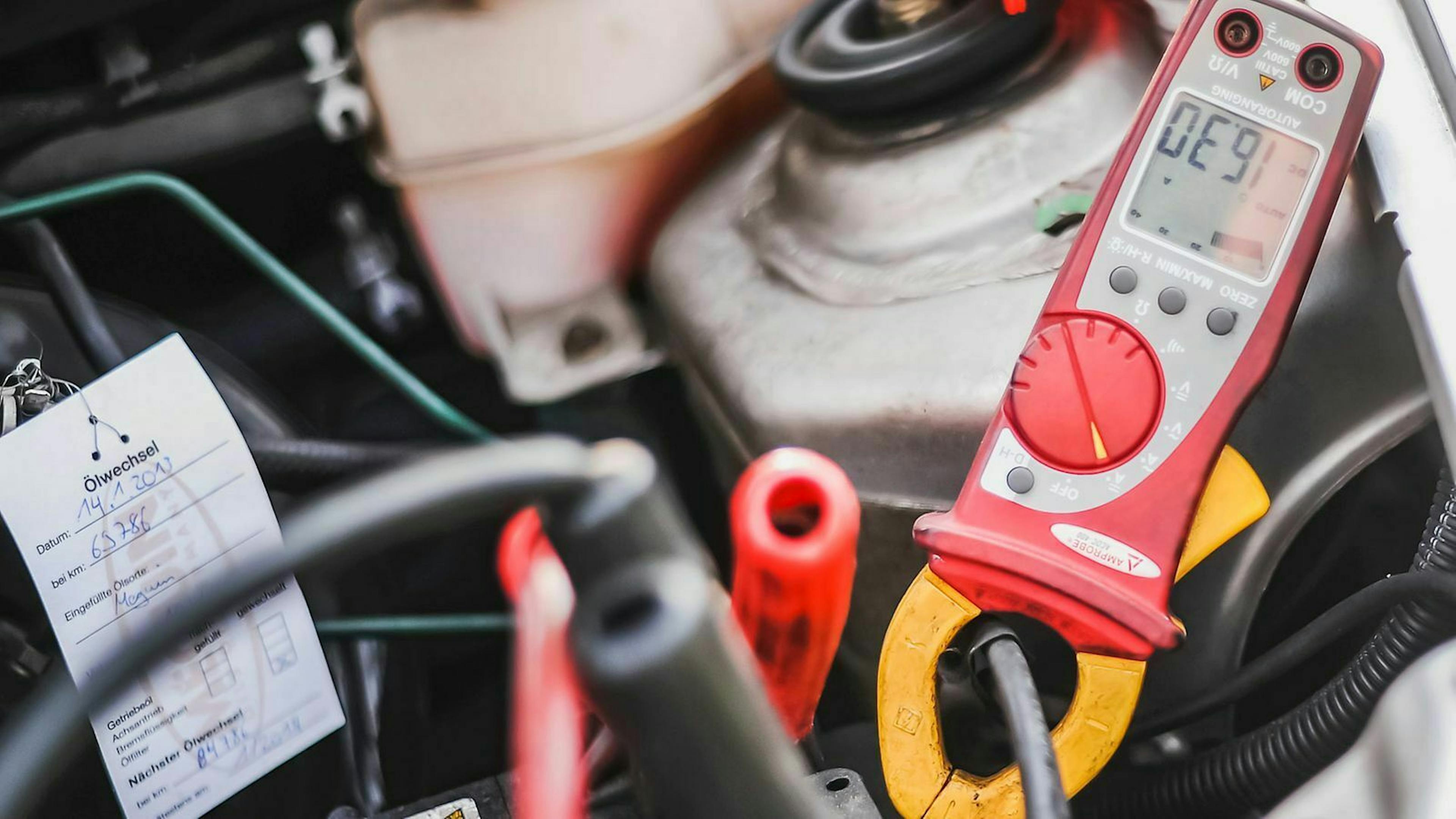 Ein Spannungsmesser klemmt an einer Autobatterie im Motorraum.