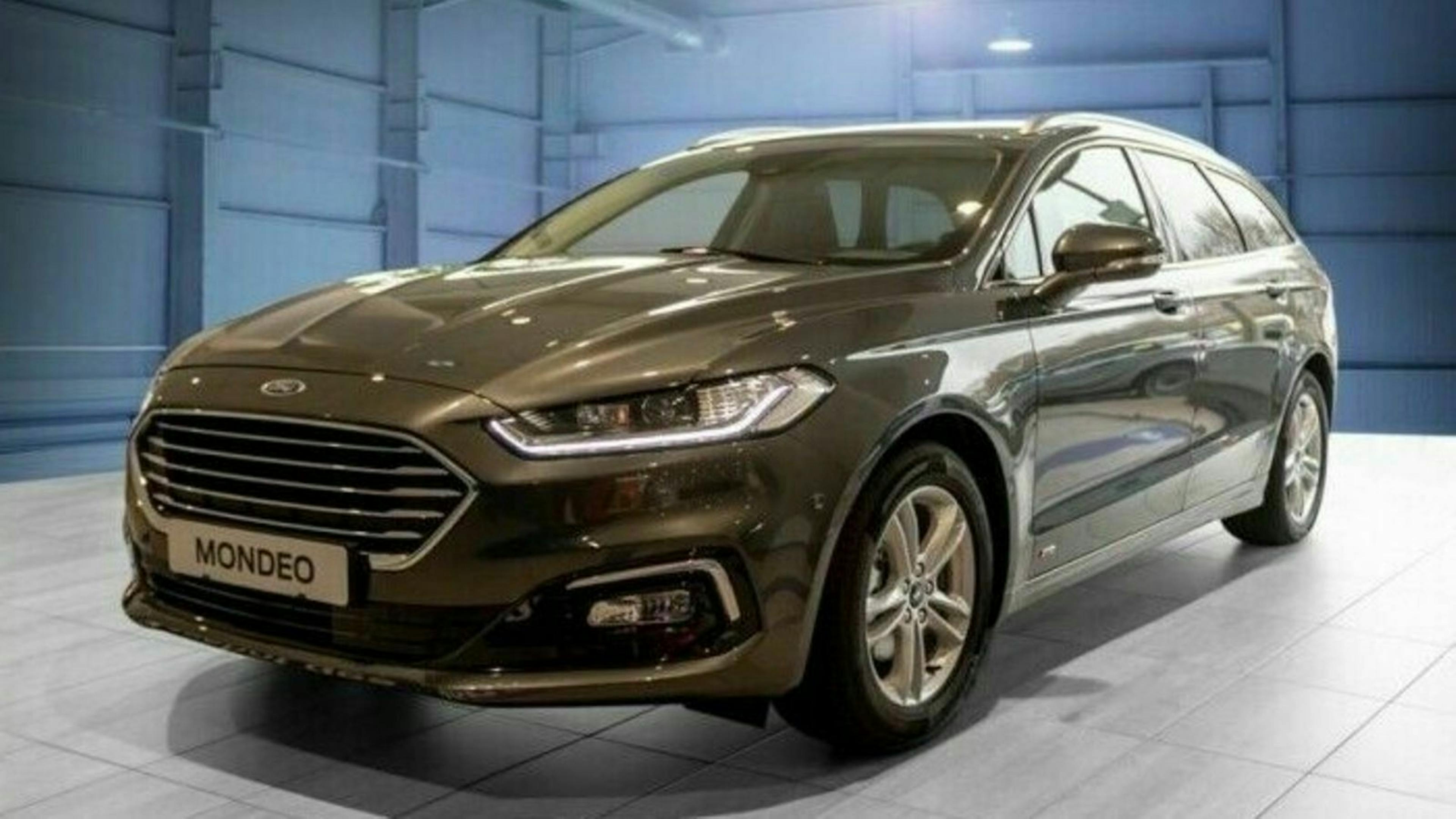 Brauner Ford Mondeo Kombi in einem hellen Raum mit modernen Design-Elementen, seitliche Ansicht mit sichtbaren Frontleuchten und Kühlergrill.