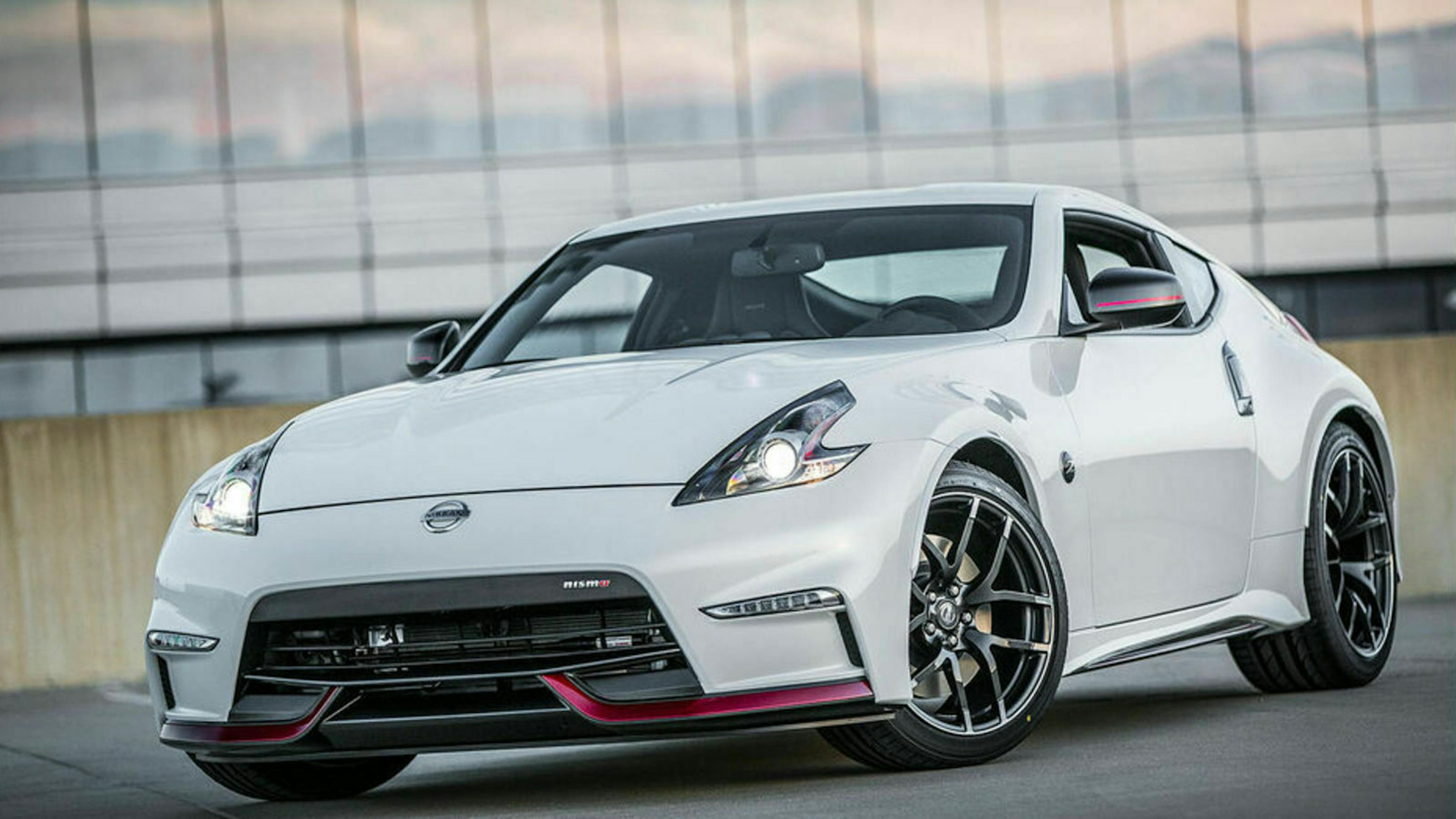 Ein weißer Nissan 370Z steht auf einem Platz vor einer Glasfassade
