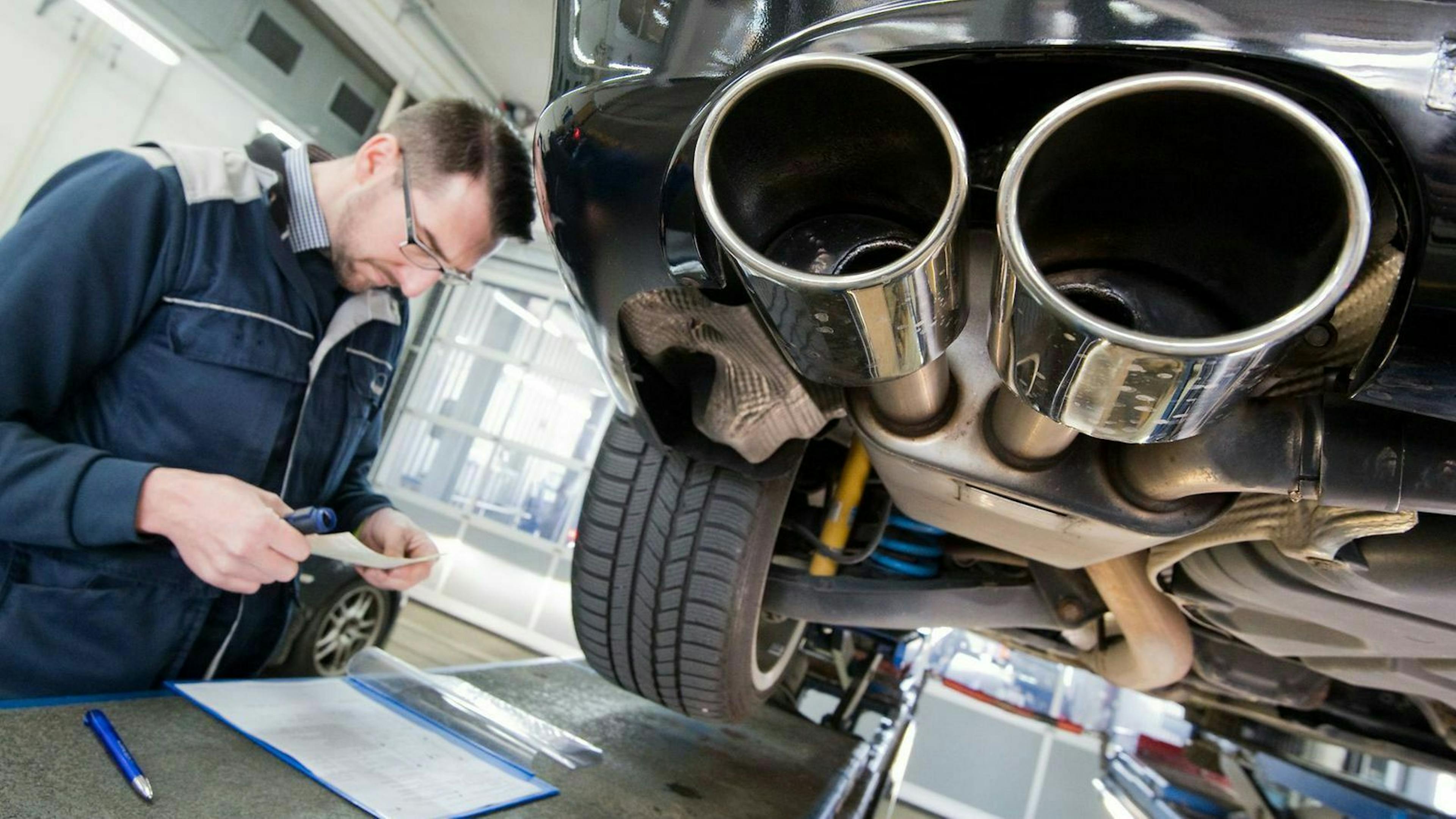 Mann steht vor einem Auto und schaut auf einen Fahrzeugschein.