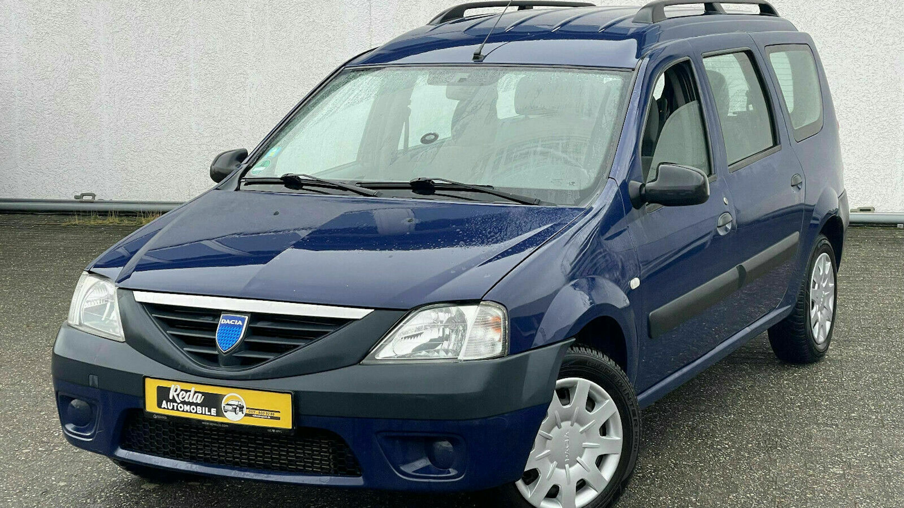 Ein blauer Dacia Logan Kombi steht vor einer weißen Wand