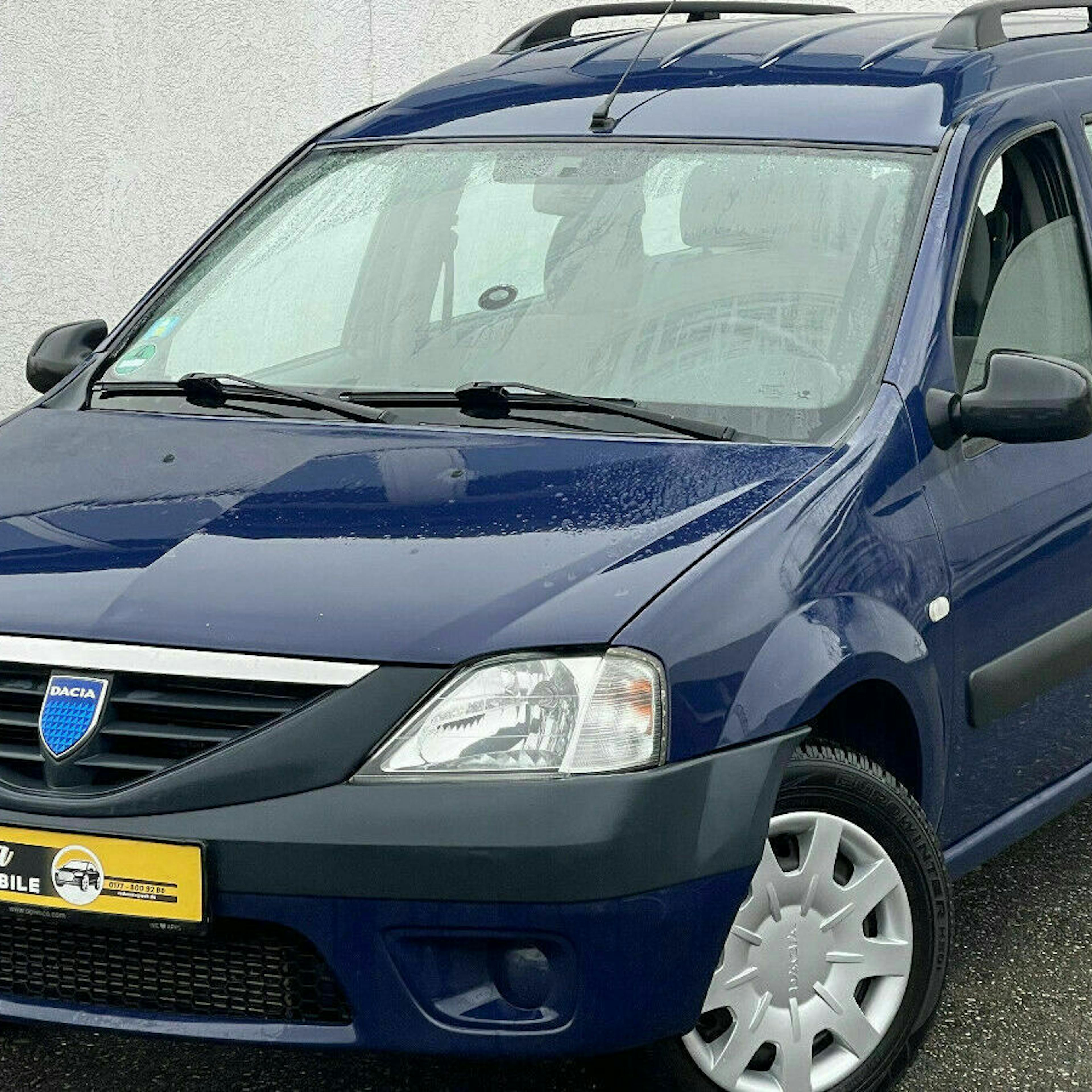 Ein blauer Dacia Logan Kombi steht vor einer weißen Wand