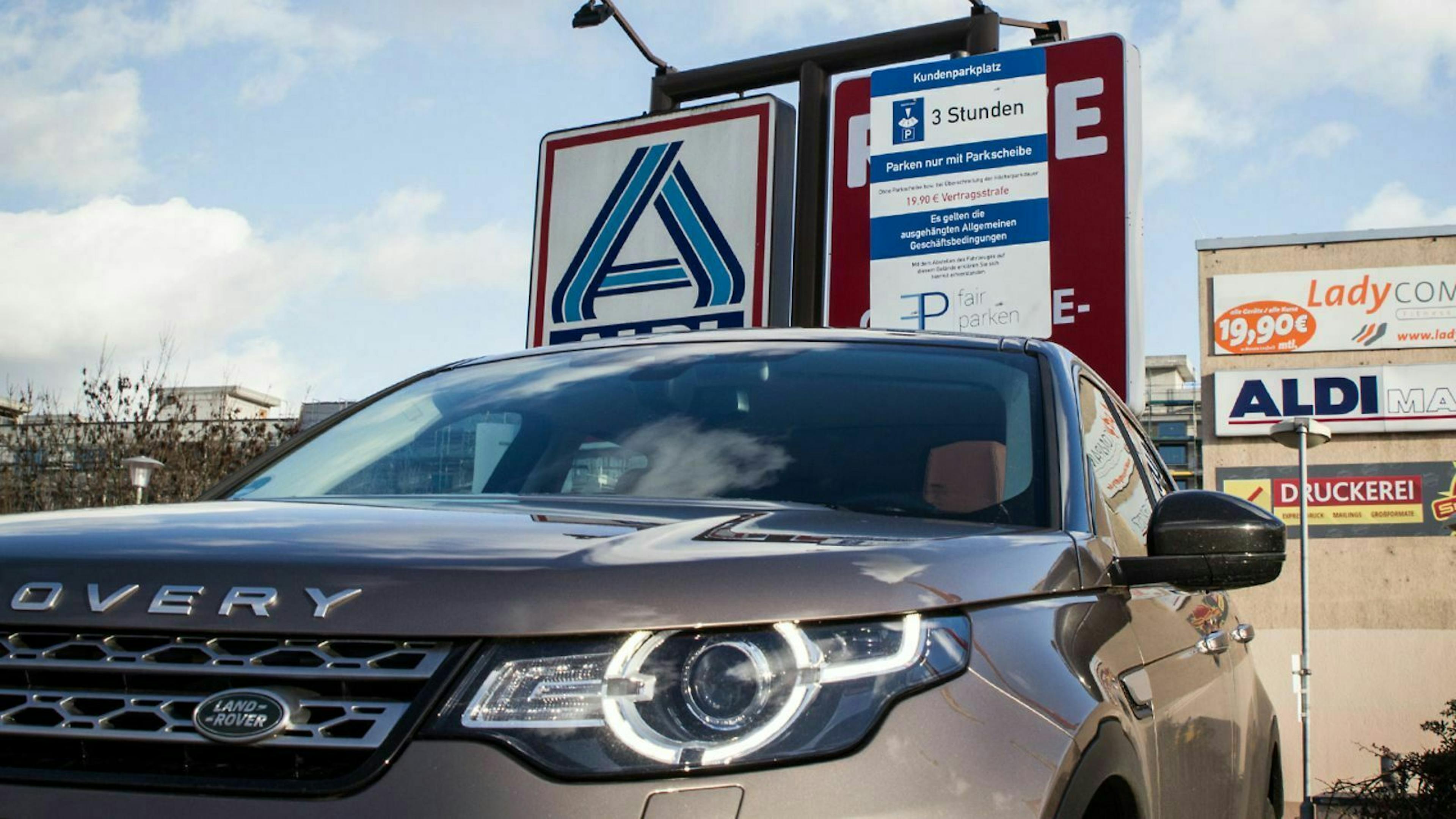 Parkplatz mit Hinweisschild. Im Vordergrund ein parkender Land Rover