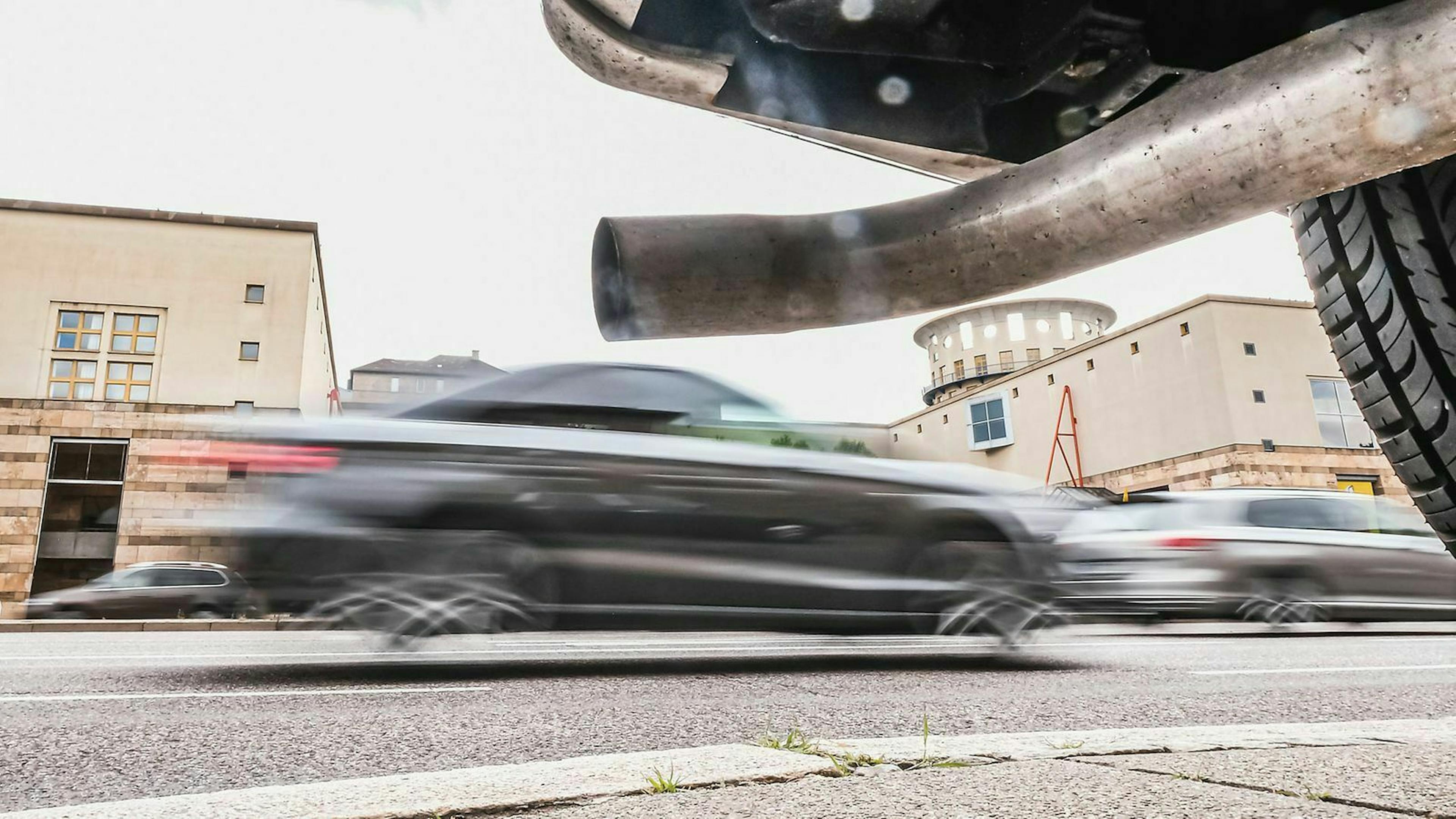 Ein Auto fährt an einem parkenden Auto vorbei dessen Auspuff zu sehen ist.