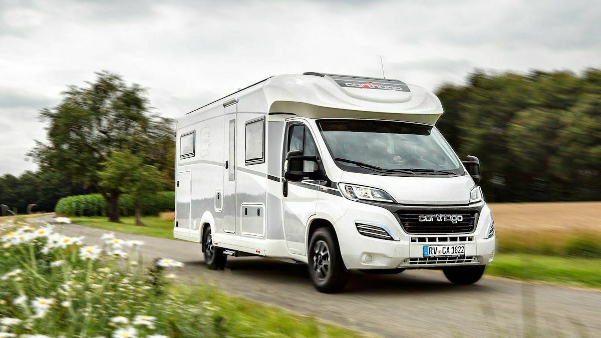 Ein weißes Carthago c-tourer T Lightweight Wohnmobil fährt eine Landstraße entlang.