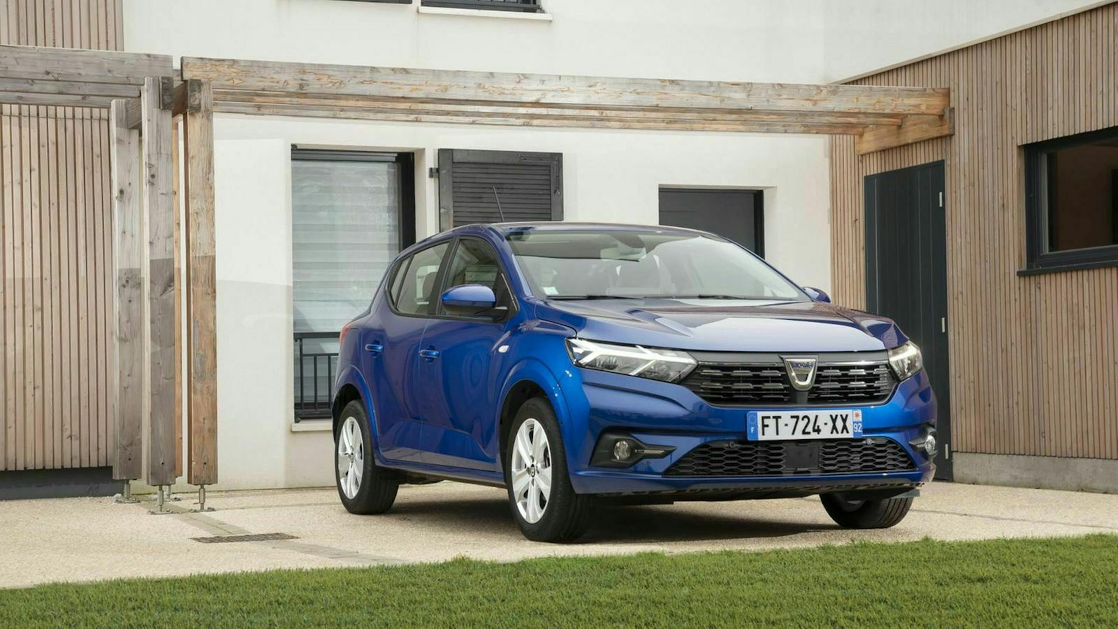 Ein blauer Dacia Sandero parkt vor einem Haus mit heller Fassade.