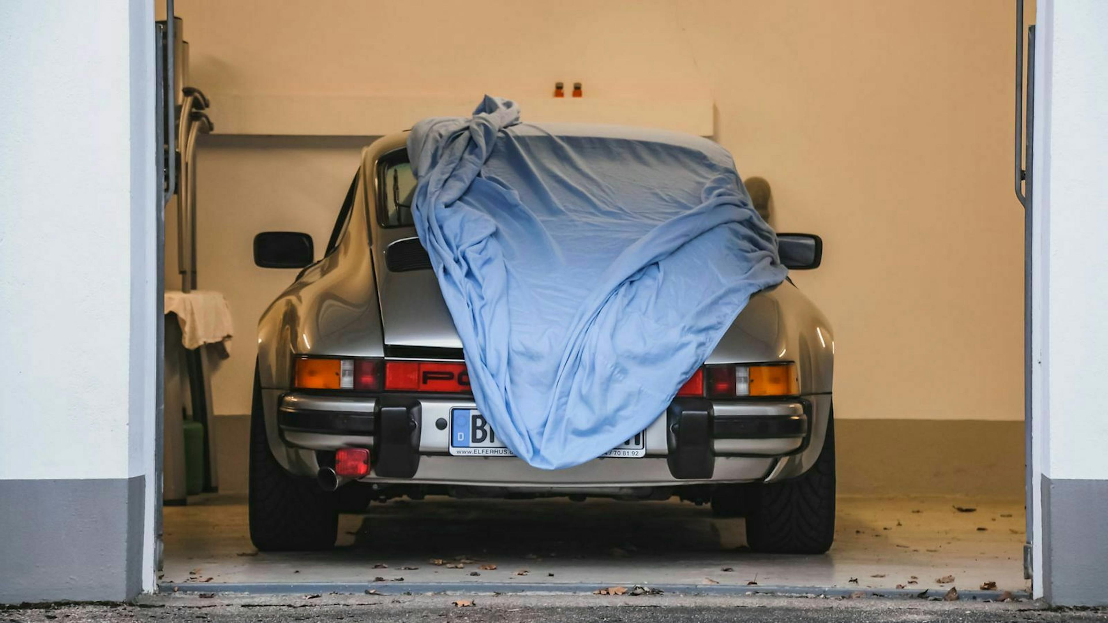 Ein silberner Porsche steht mit dem Heck zum Tor in einer Garage, halb von einem Tuch verdeckt.
