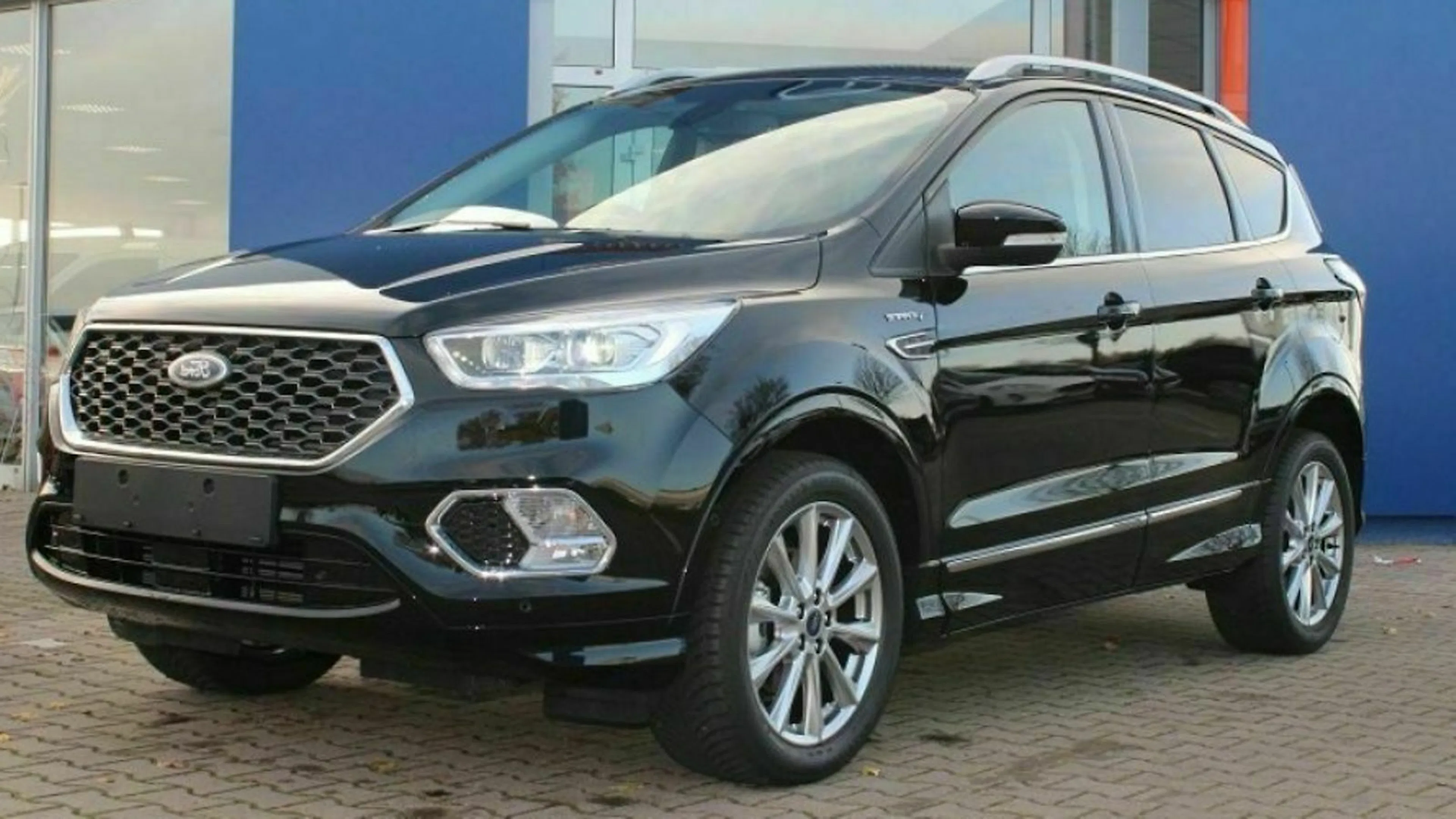 Schwarzer SUV mit glänzenden Felgen und markantem Kühlergrill, geparkt vor einem blauen Gebäude.