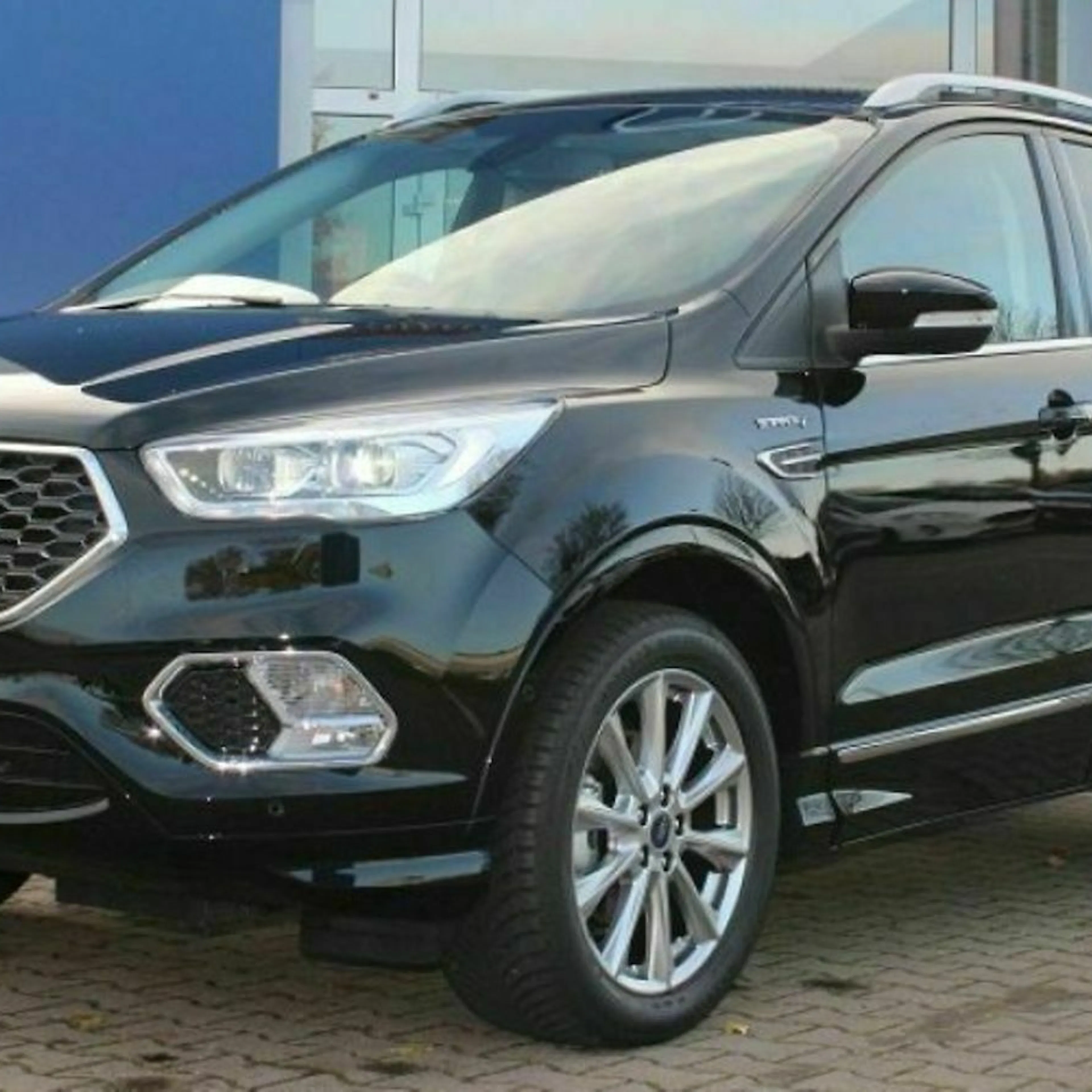 Schwarzer SUV mit glänzenden Felgen und markantem Kühlergrill, geparkt vor einem blauen Gebäude.