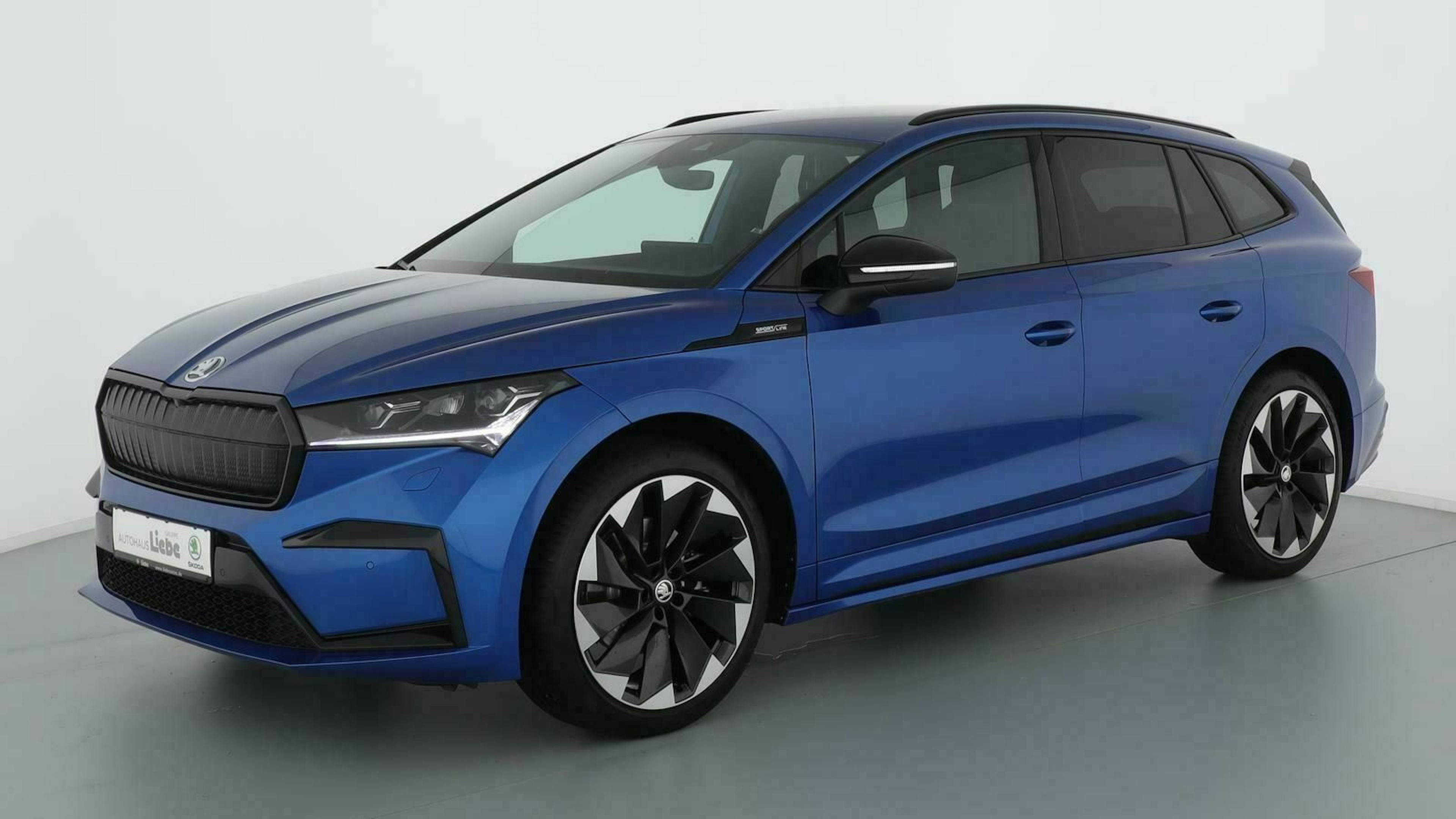 Ein blauer Skoda Enyaq iV steht vor einer weißen Wand