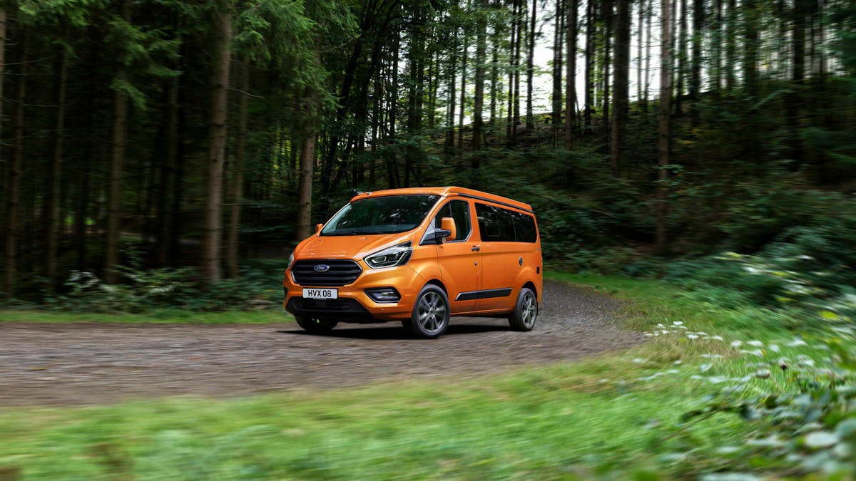 Ein orangefarbener Ford Nugget fährt durch einen Wald
