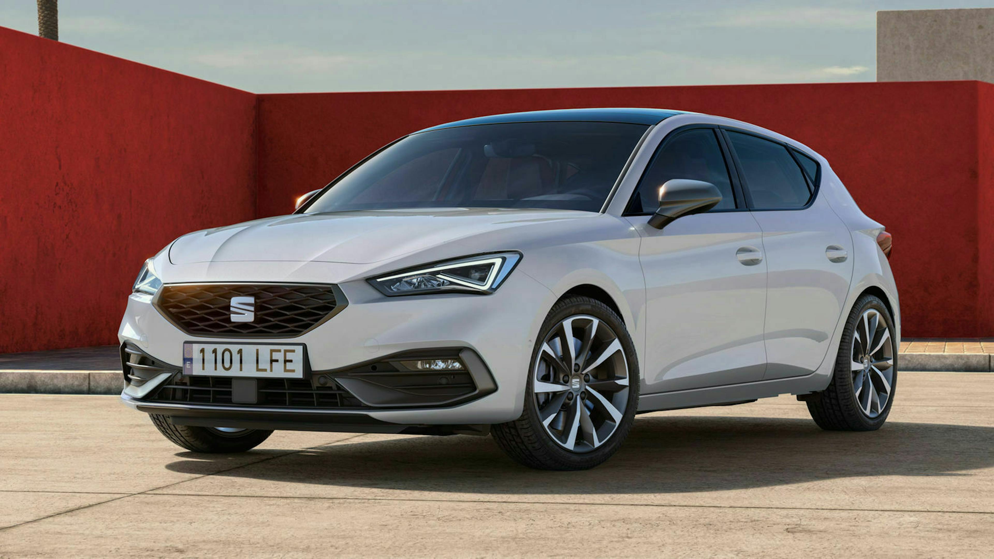 Ein weißer Seat Leon steht auf einem Parkplatz vor einer roten Wand