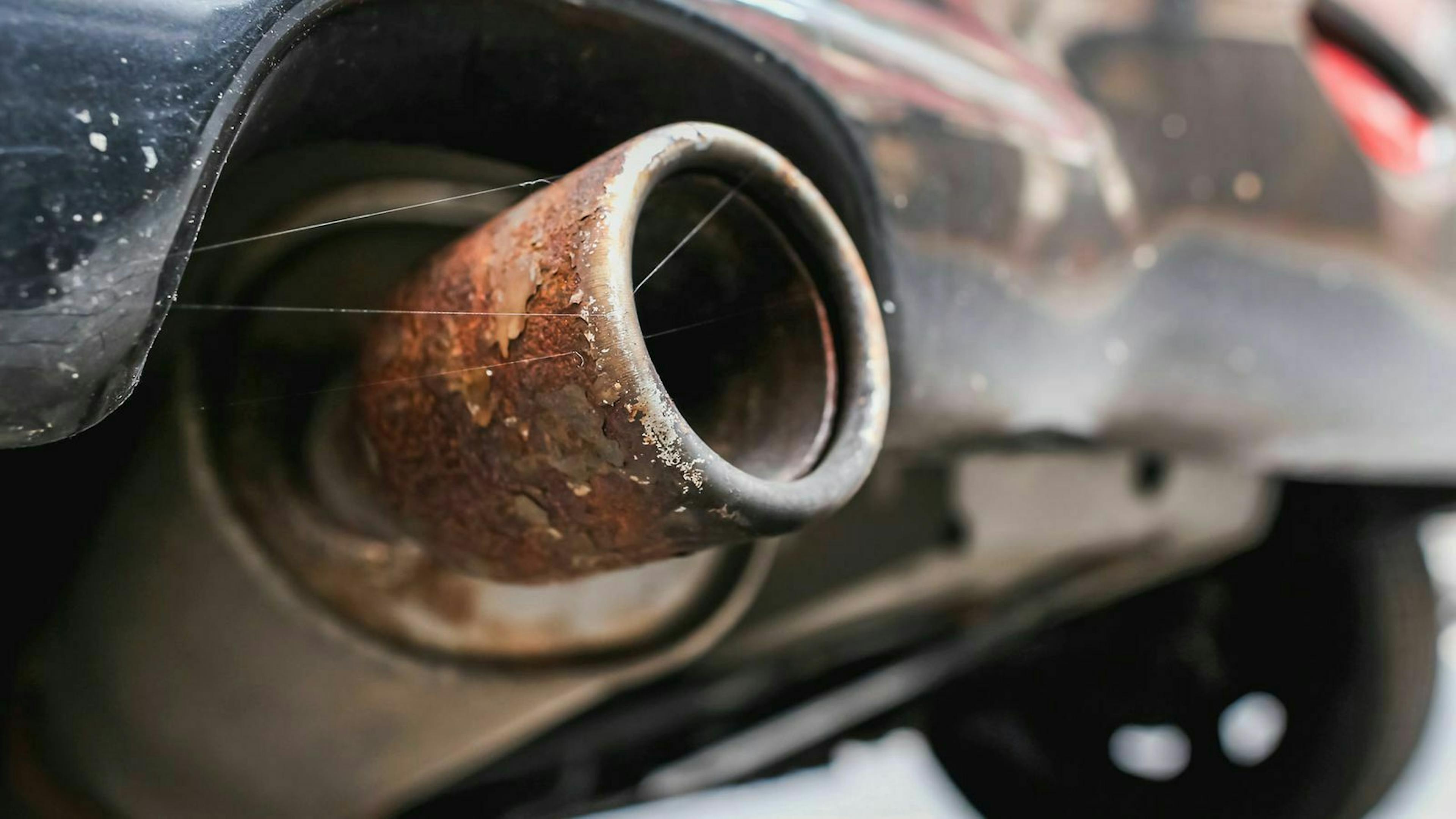 Unter einem Auto ragt der rostende Auspuff hervor.