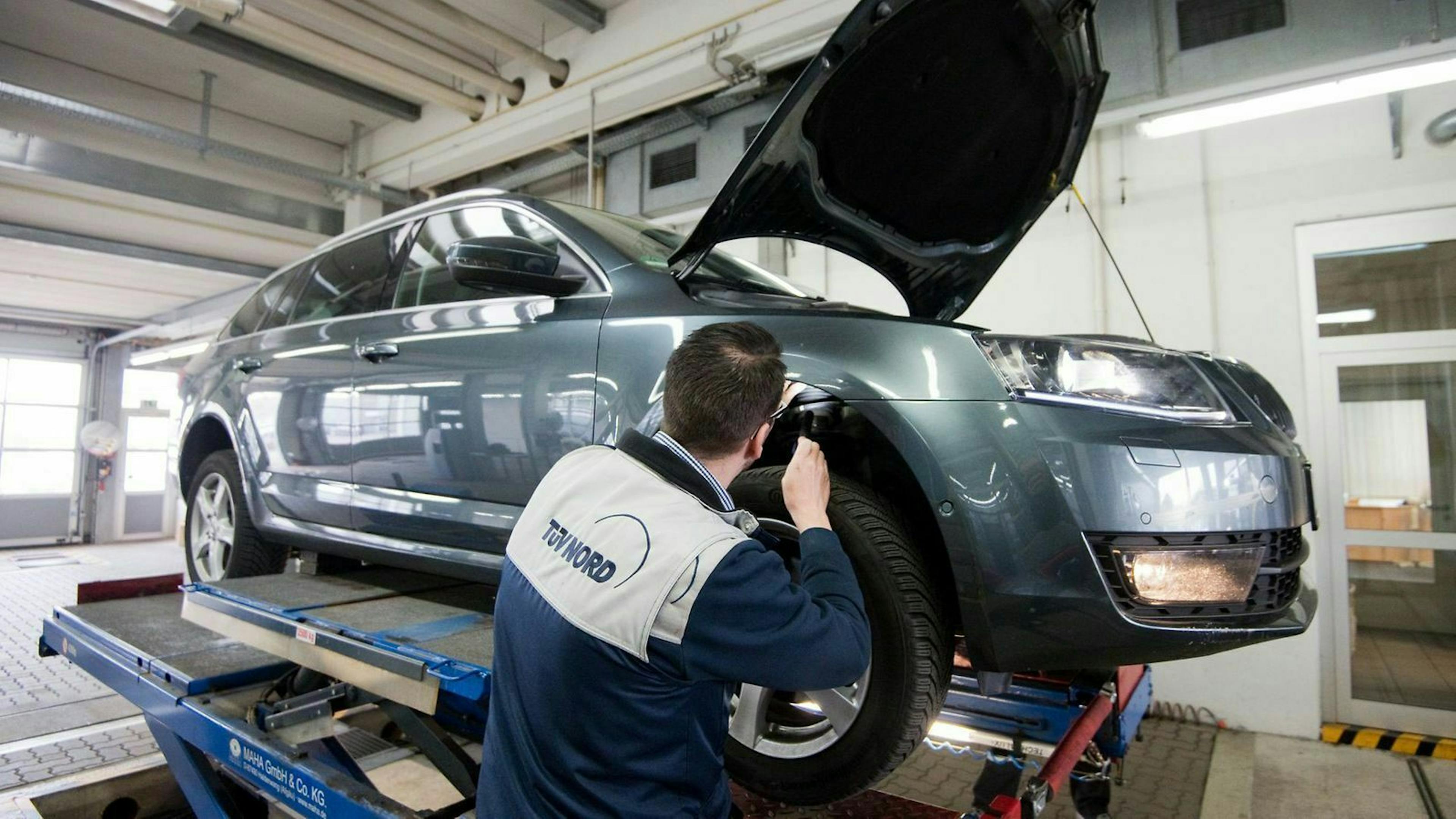 TÜV-Prüfer kontrolliert mit einer Taschenlampe den Radkasten eines Autos.