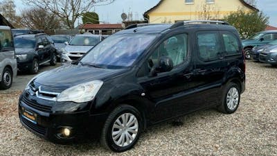 Ein schwarzer Citroen Berlingo steht auf einem Parkplatz vor einem gelben Haus