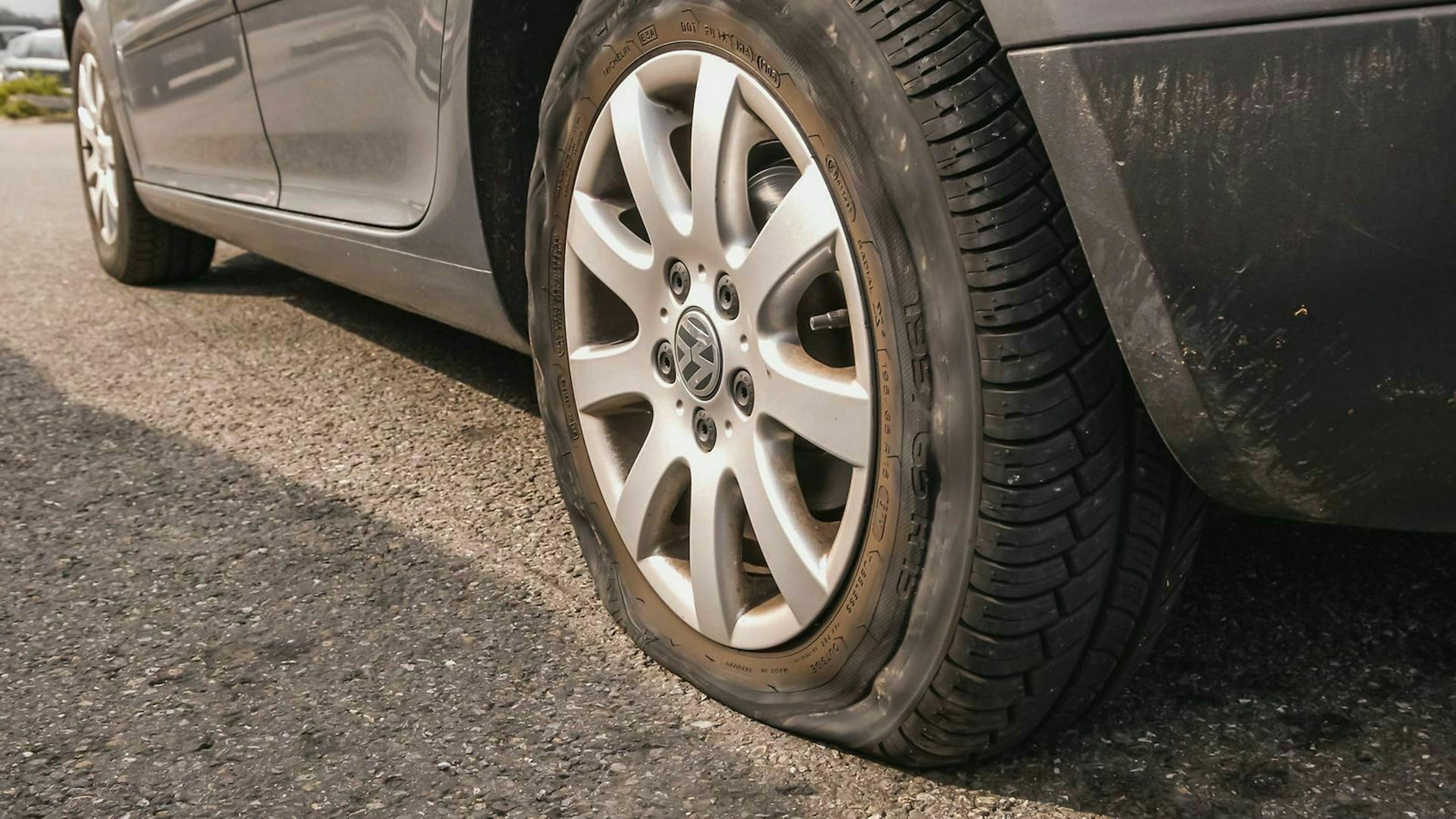Ein graues Auto wird durch einen platten Reifen an der Weiterfahrt gehindert.
