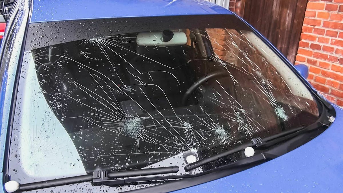 Die Windschutzscheibe eines blauen Autos ist durchzogen mit Rissen resultierend aus Steinschlägen