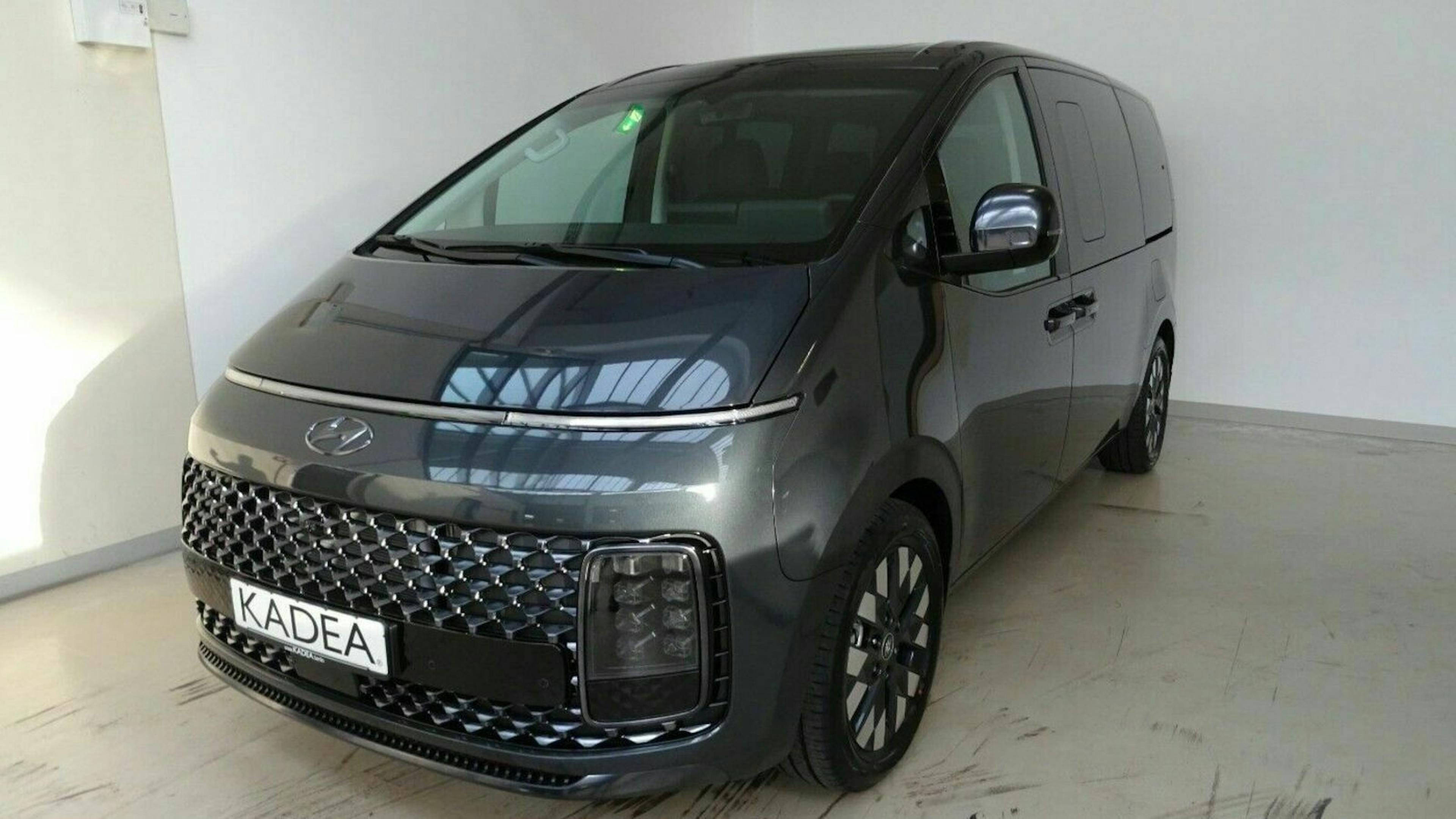 Ein grauer Hyundai Staria steht vor einer weißen Wand