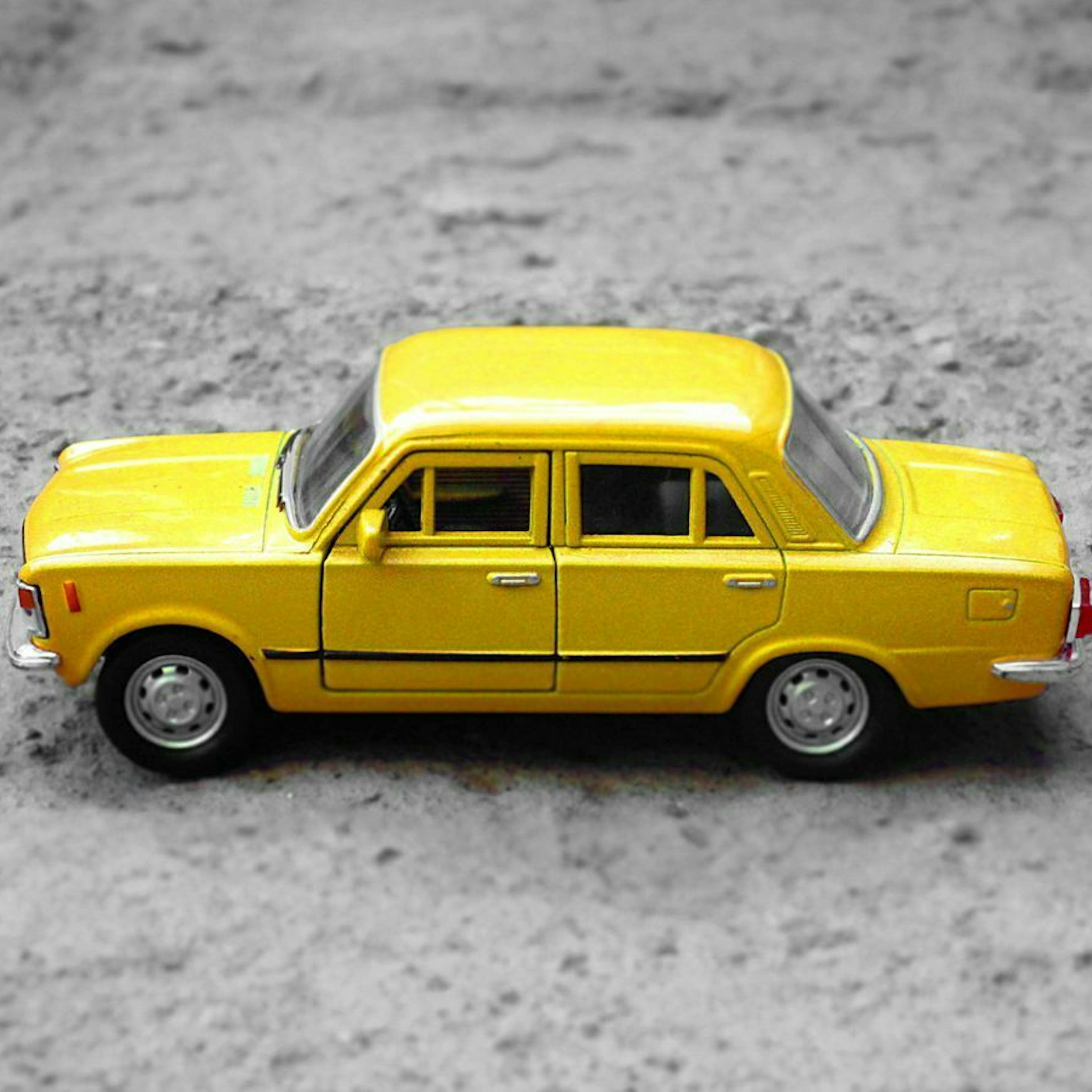 Ein gelbes Spielzeugauto steht auf einem grauen Steinboden