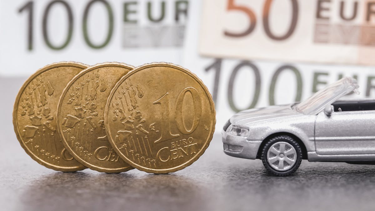 Ein silbernes Modellauto parkt neben aufrecht stehenden 10-Cent-Münzen