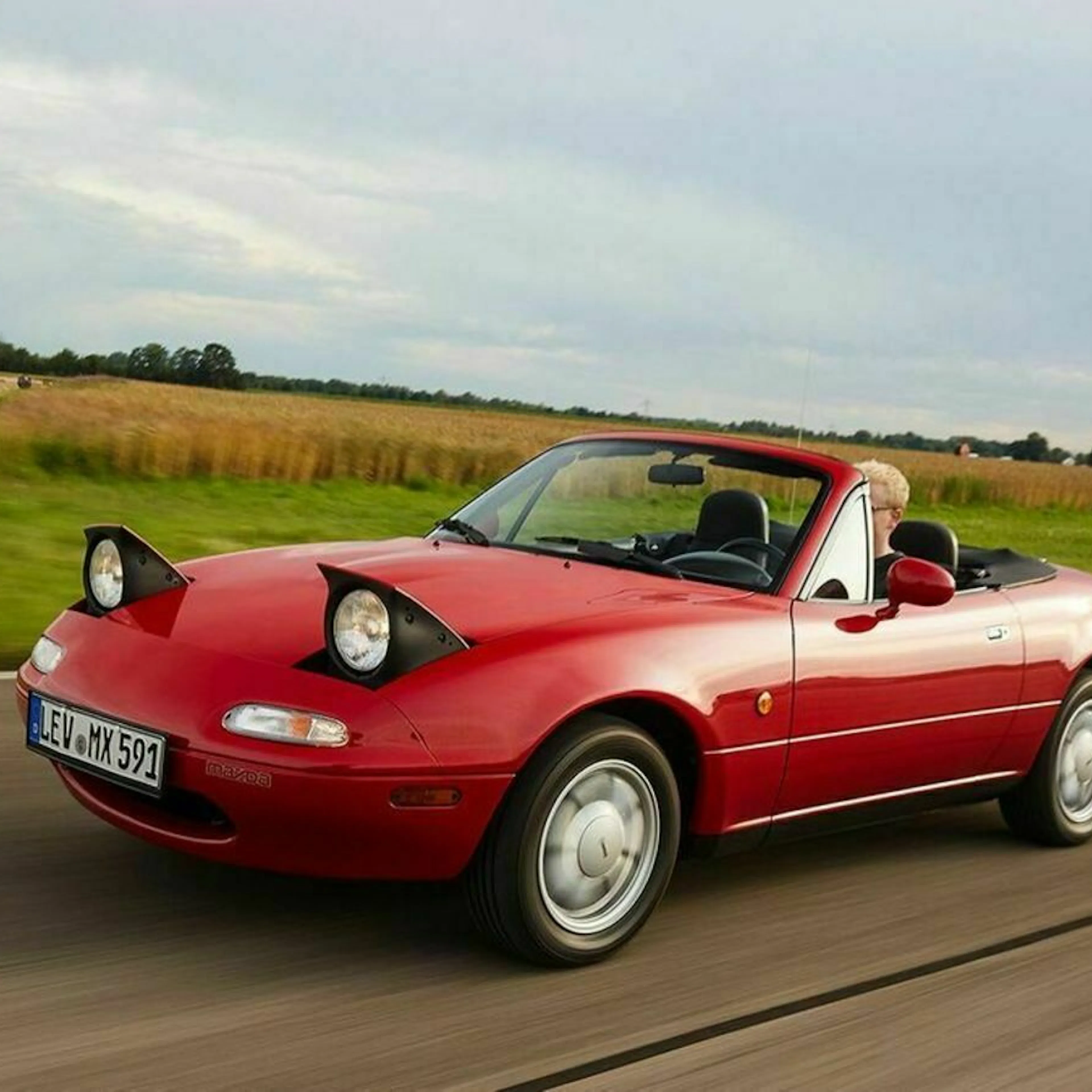 Ein rotes Madza MX-4 NA Cabrio fährt eine Landstraße entlang