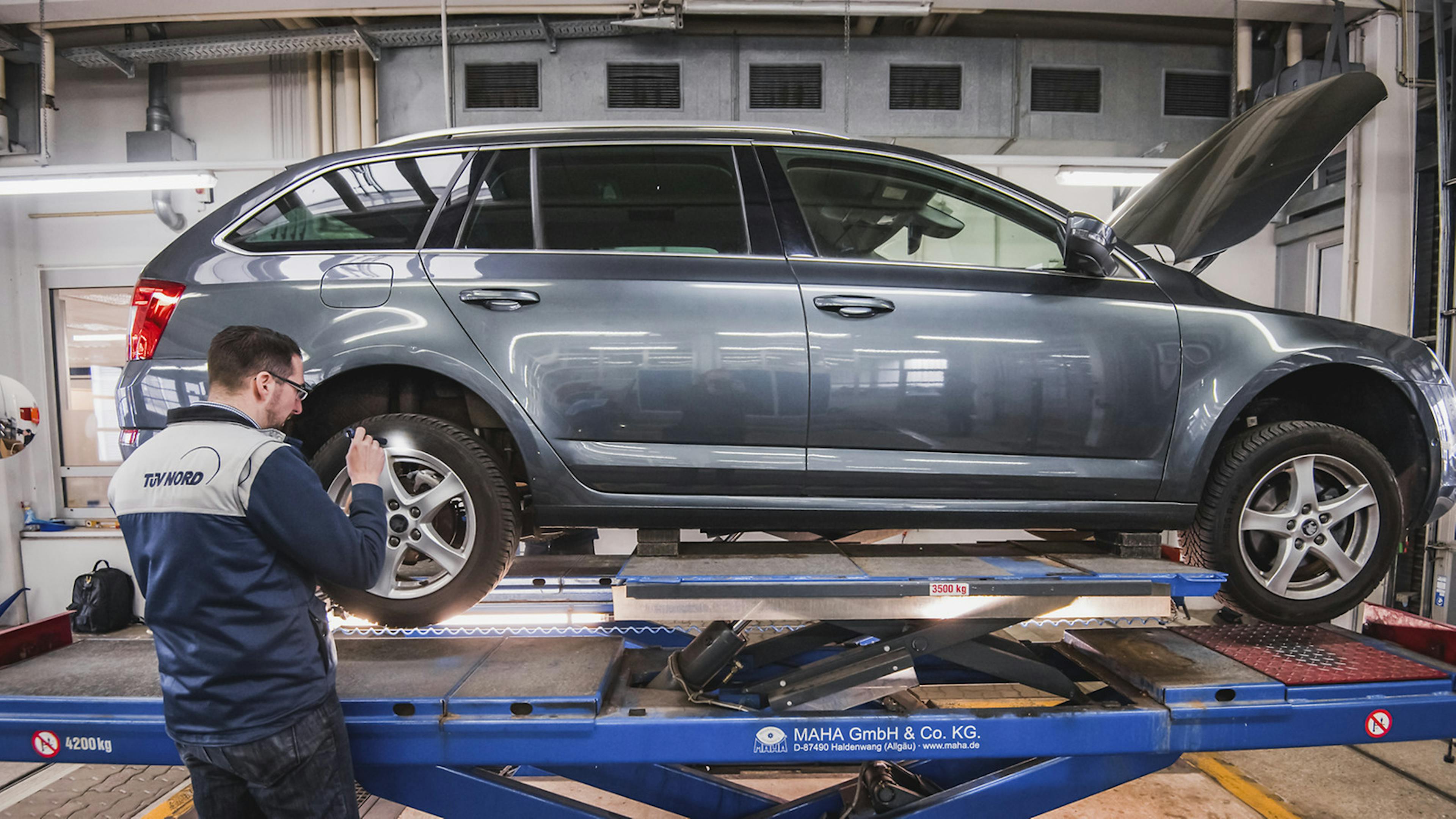 Ein Mitarbeiter des TÜV untersucht ein Auto auf einer Hebebühne.