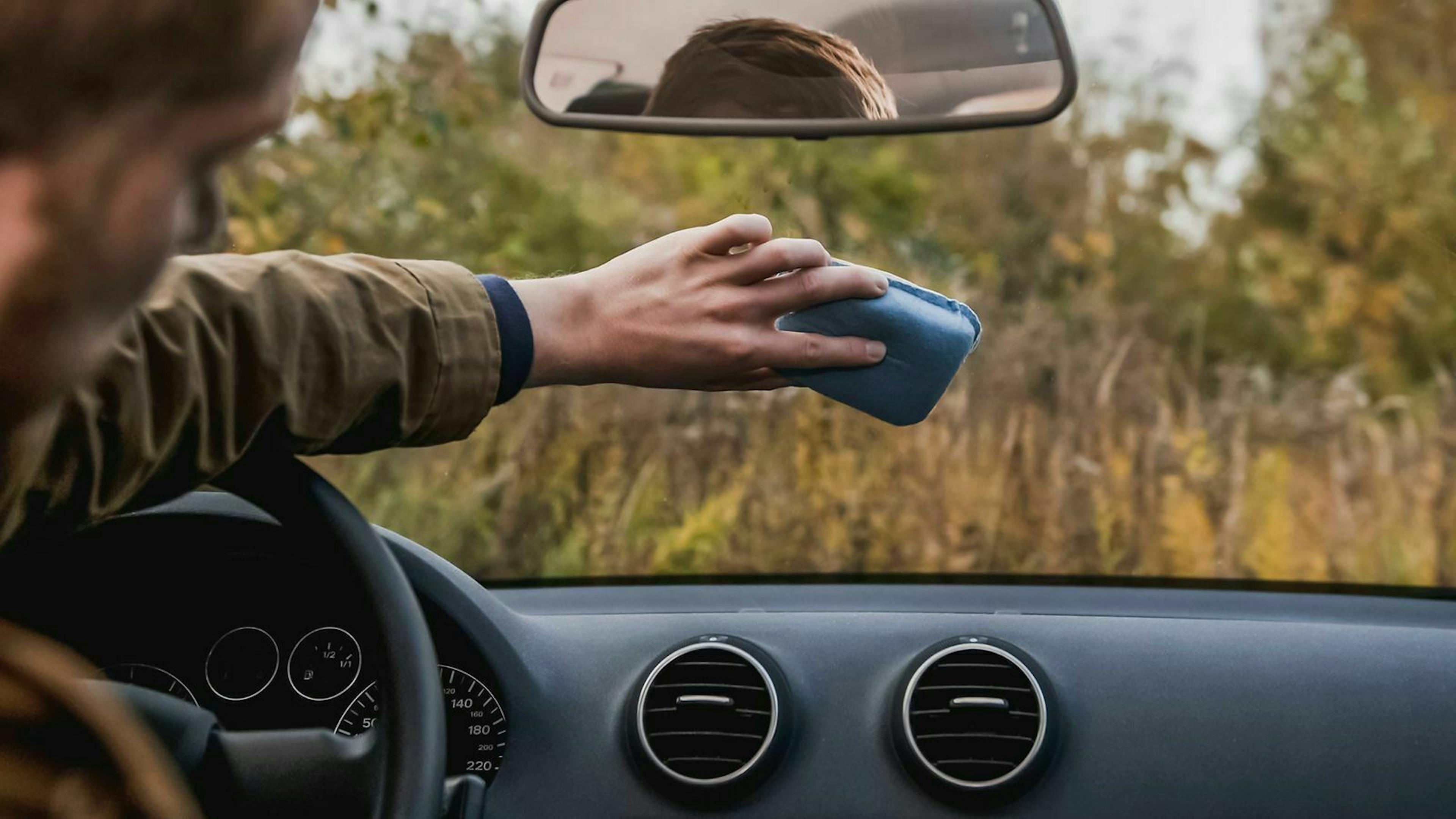 Ein Mann putzt die Innenseite der Windschutzscheibe seines Autos.