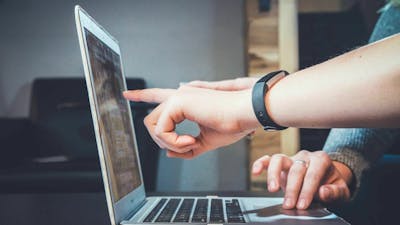Nahaufnahme von zwei Personen, die an einem aufgeklappten Laptop arbeiten