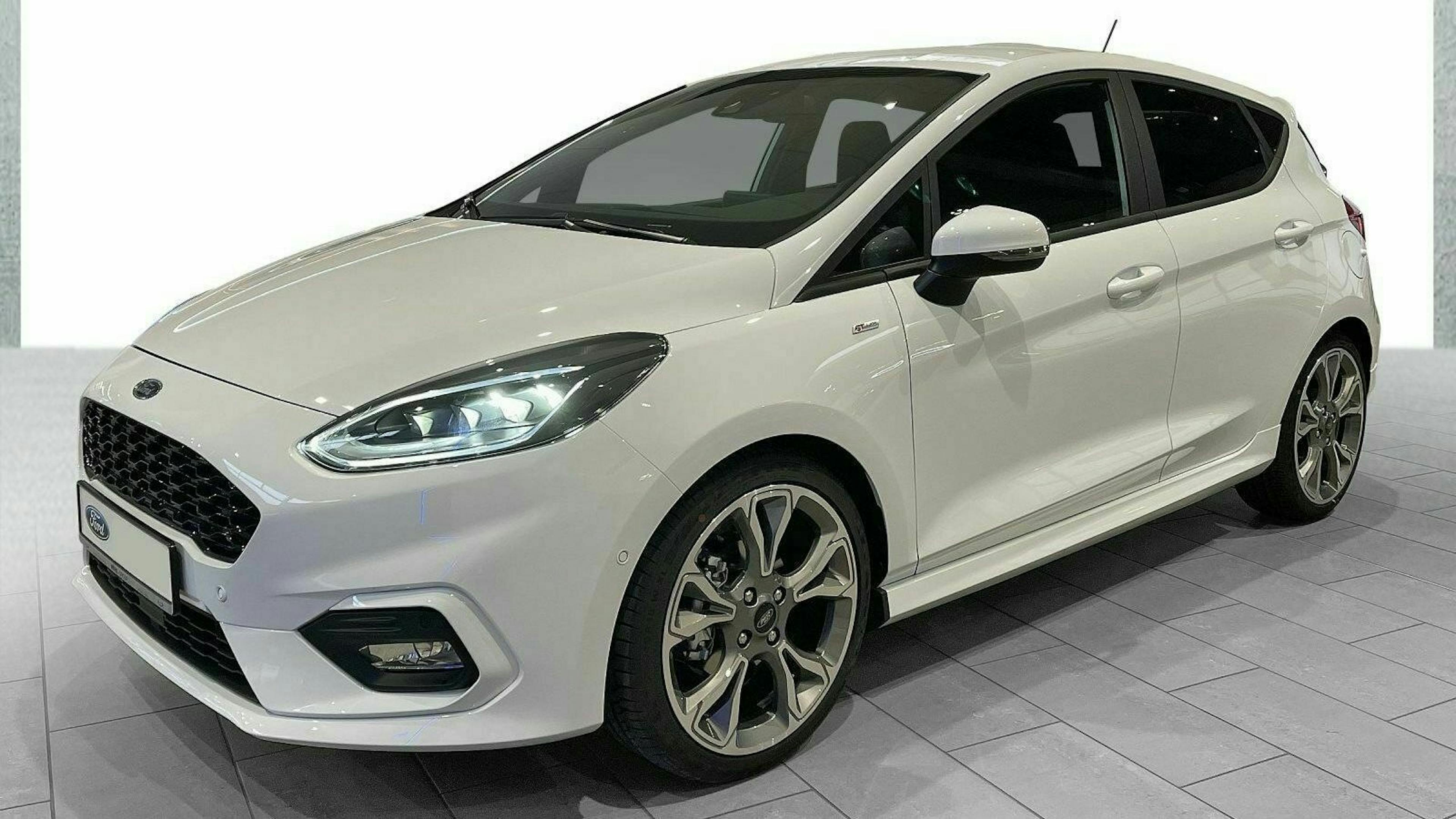 Weißer Ford Fiesta in Seitenansicht, geparkt auf grauem Boden. Moderne Scheinwerfer und sportliche Felgen sind gut sichtbar.
