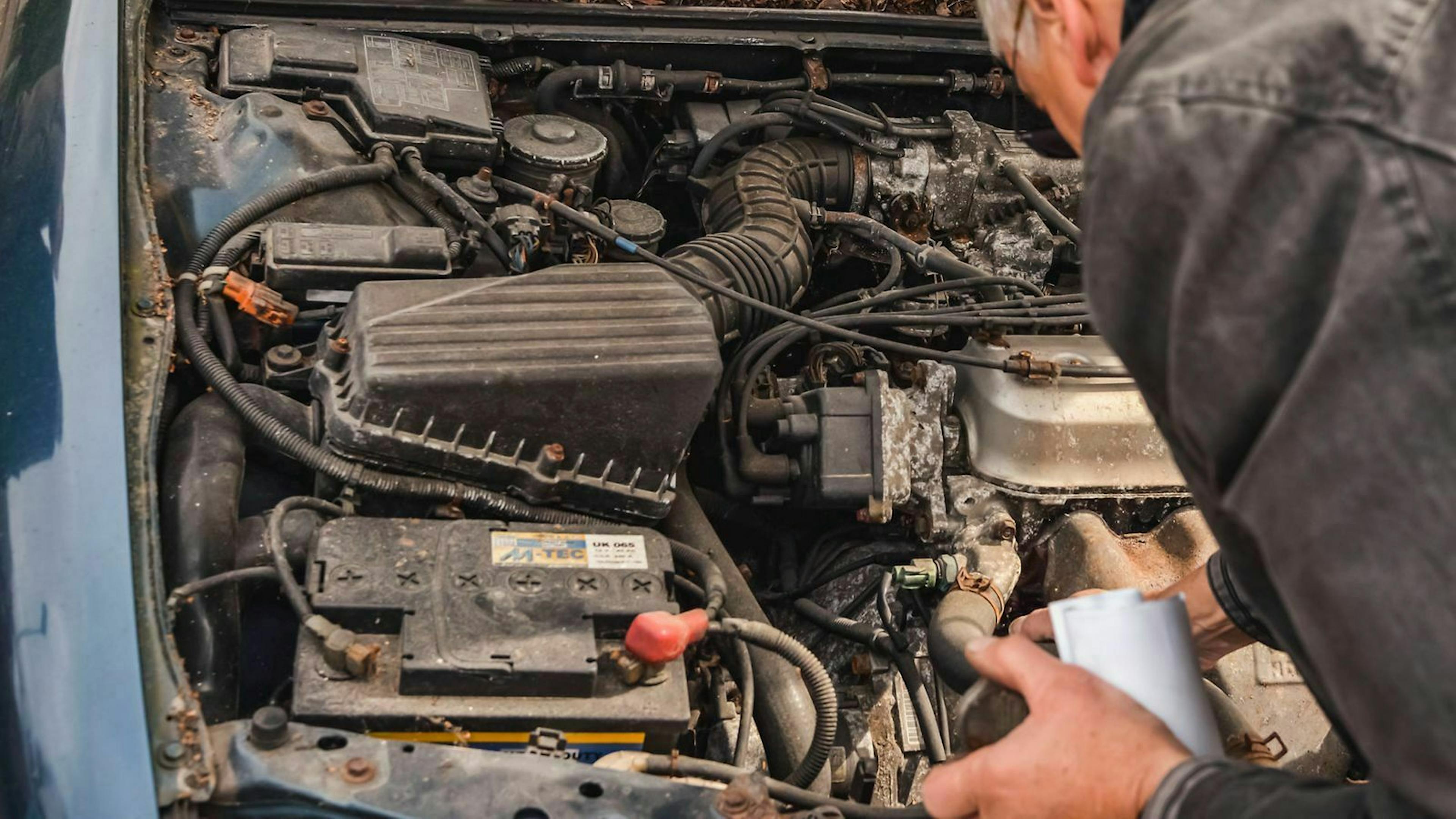 Jemand blickt in den Motorraum eines Gebrauchtwagen, bei dem der Keilreiemen gewechselt werden muss.