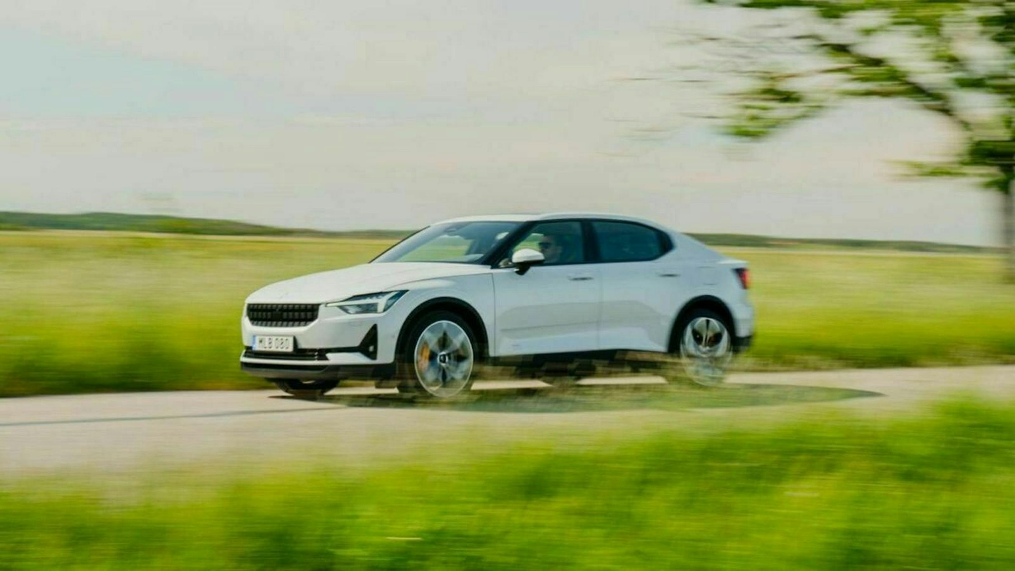 Ein weißer PKW fährt eine Landstraße entlang an grünen Feldern vorbei