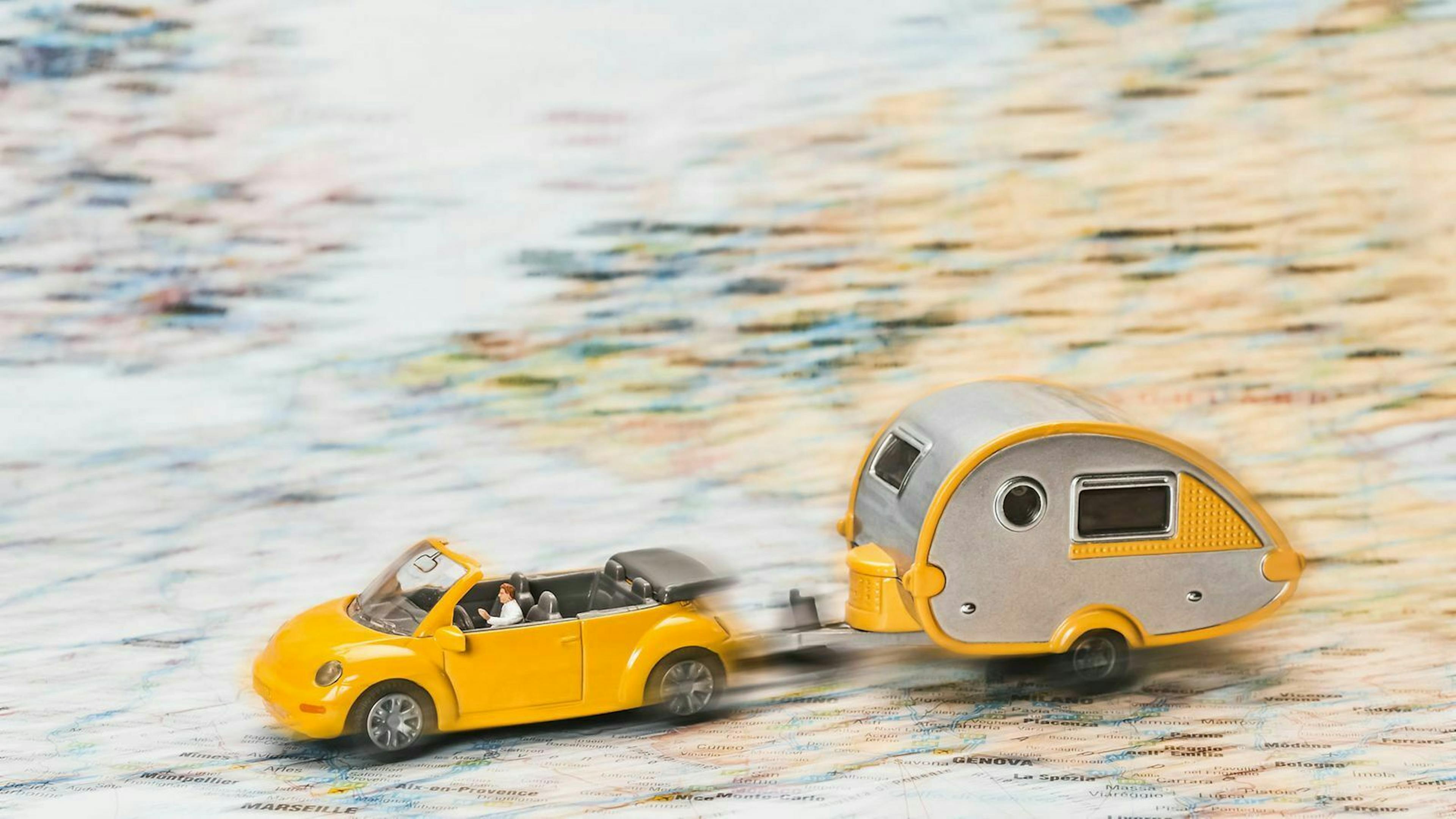 Ein Modellauto zieht einen Miniatur-Wohnanhänger über eine Landkarte.