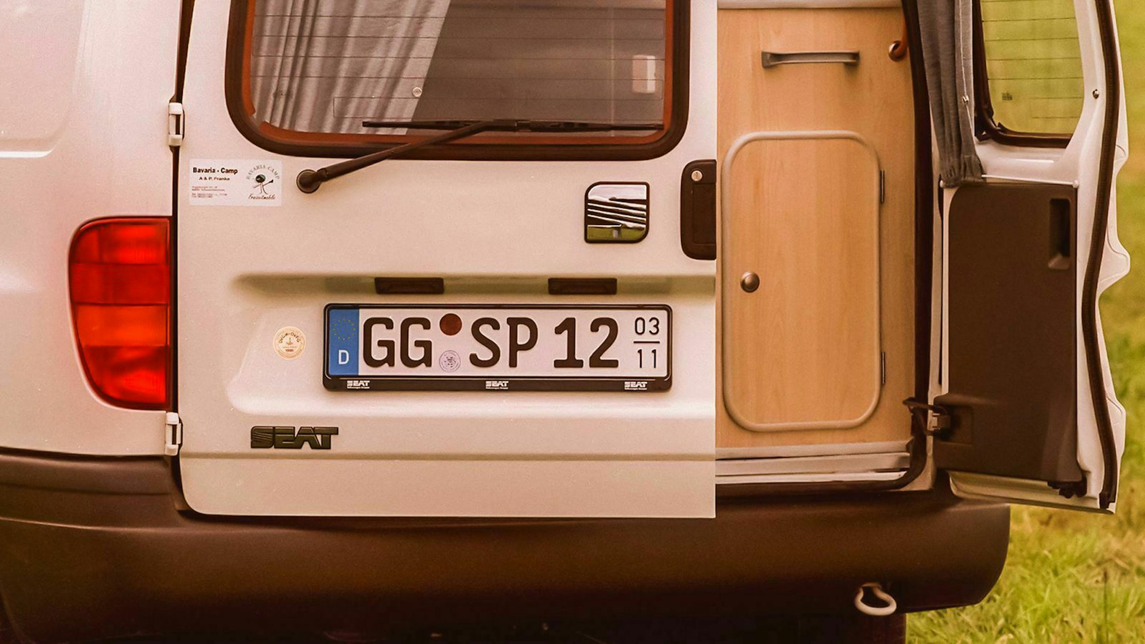 Ein weißer Camper mit Saisonkennzeichen steht mit offener Heckklappe auf einem Parkplatz.