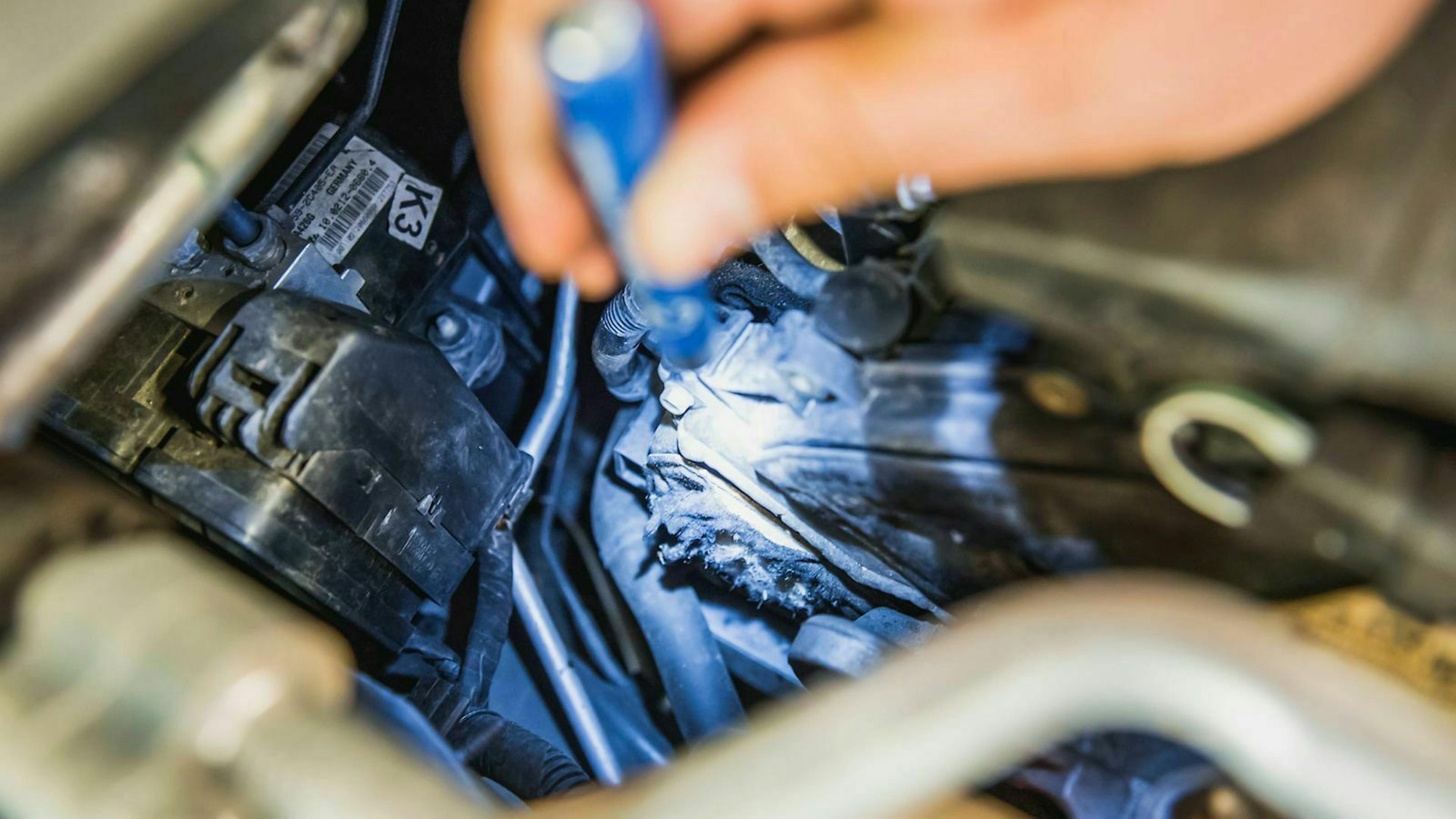 Jemand leuchtet in einen Motorraum und entdeckt einen Marderschaden.