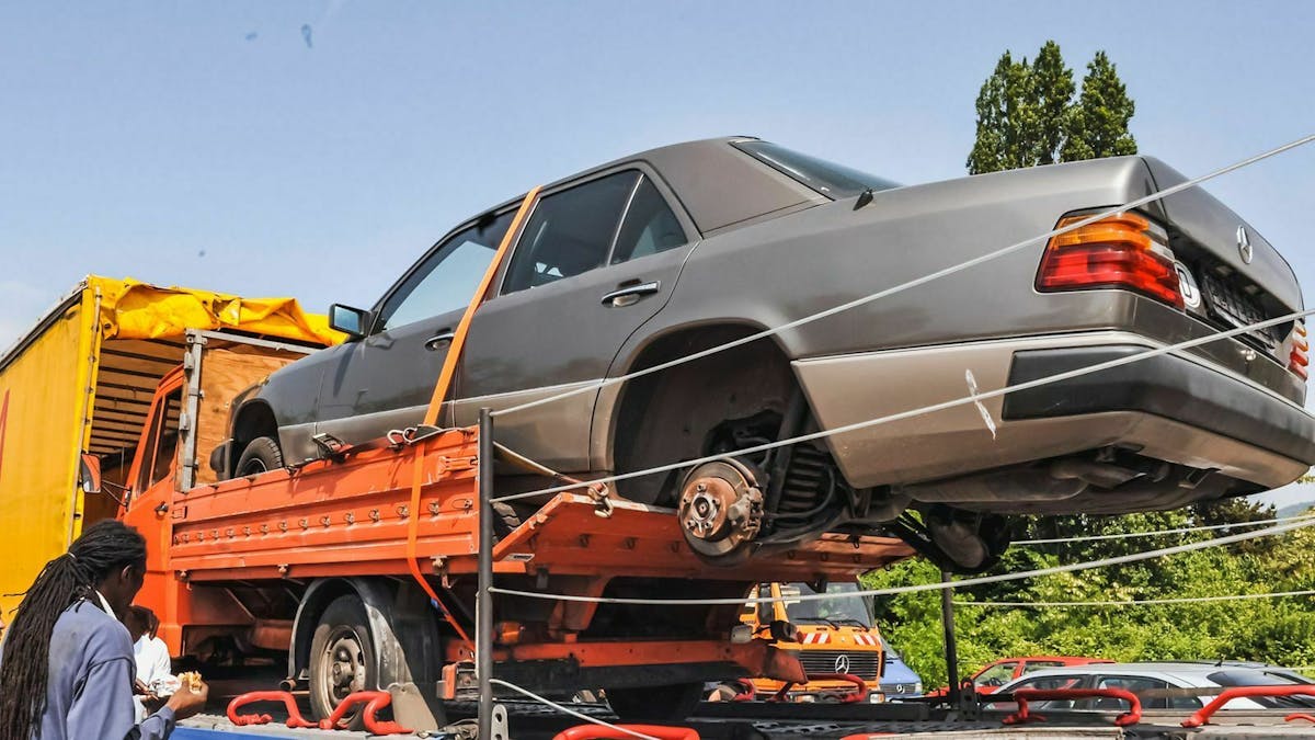 Ein Auto ohne Räder auf der Pritsche eines kleinen Transporters soll gerade in einen Lkw geladen werden.