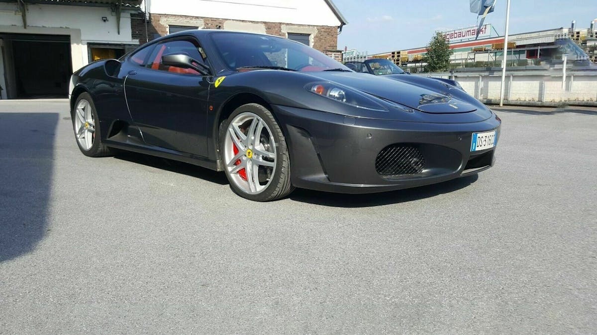 Der graue Ferrari F430 in der Ansicht von rechts-vorne, auf dem Hof eines Autohändlers stehend